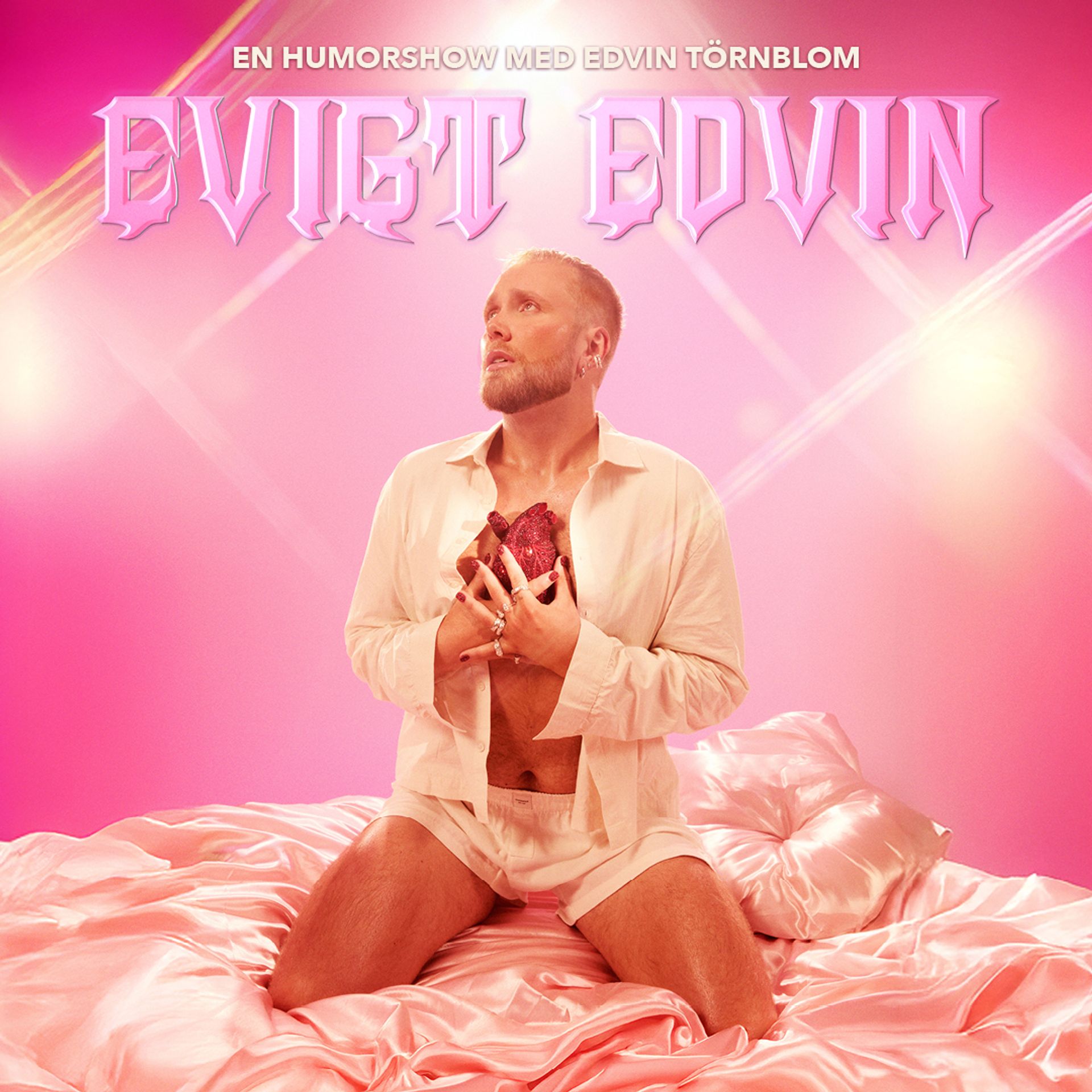 Manér bild för Eviga Edvin med Edvin Törnblom. Han sitter på en säng med siden lakan iklädd siden pyjamas shorts och en skjorta. Han håller i ett diamant hjärta. Hela bilden går i rosa färger.