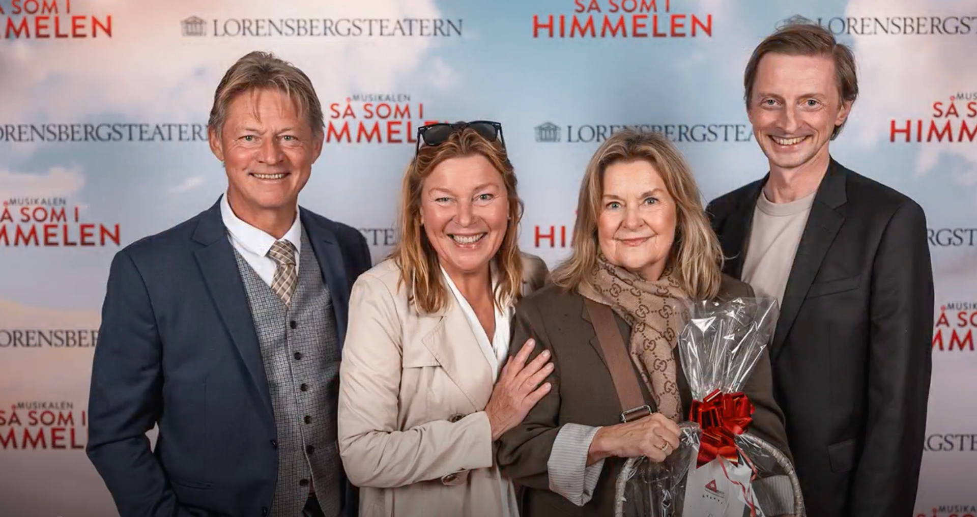 Bild från röda mattan vid premiären av musikalen Så som i himmelen på Lorensbergsteatern i Göteborg. Lotta Engberg och Mikael ”Soldoktorn” Sandström står tillsammans med två andra personer framför en fotovägg med musikalens och teaterns logotyper. Alla fyra ler mot kameran och en av personerna håller en inslagen present med röd rosett.
