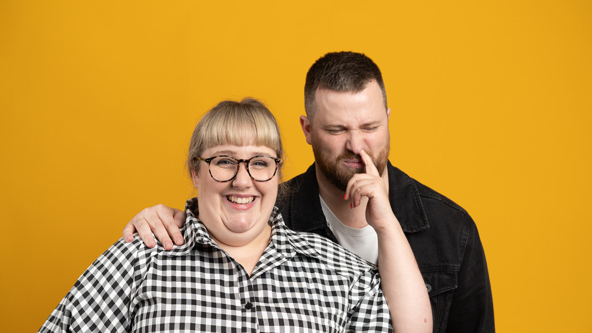 Manér för live podcasten Toni och Ryan. Toni står snett framför Ryan i en svart/vit rutig skjorta och petar Ryan som har en svart skjorta i näsan.