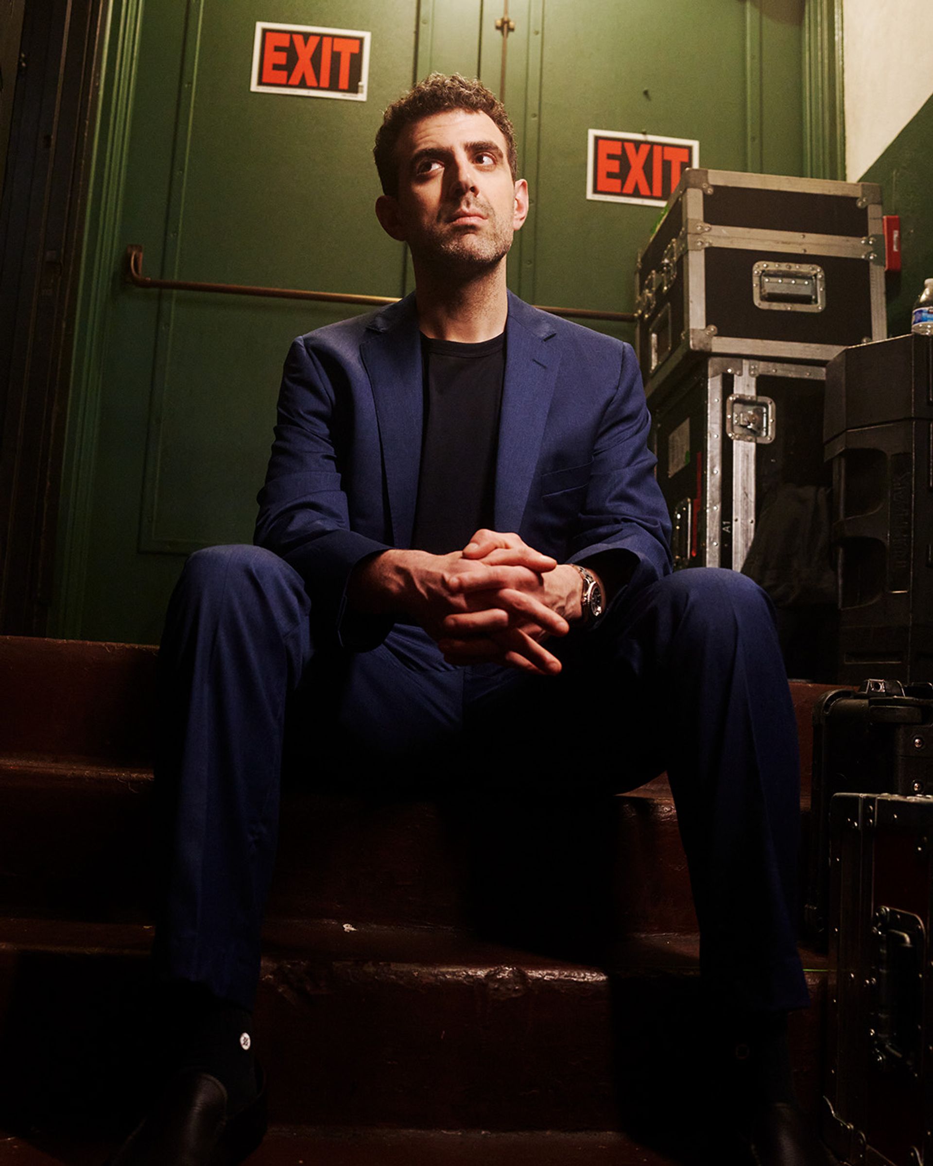 Sam Morril standup show – komiker i blå kostym bakom scen med EXIT-skyltar, porträtt inför liveföreställning