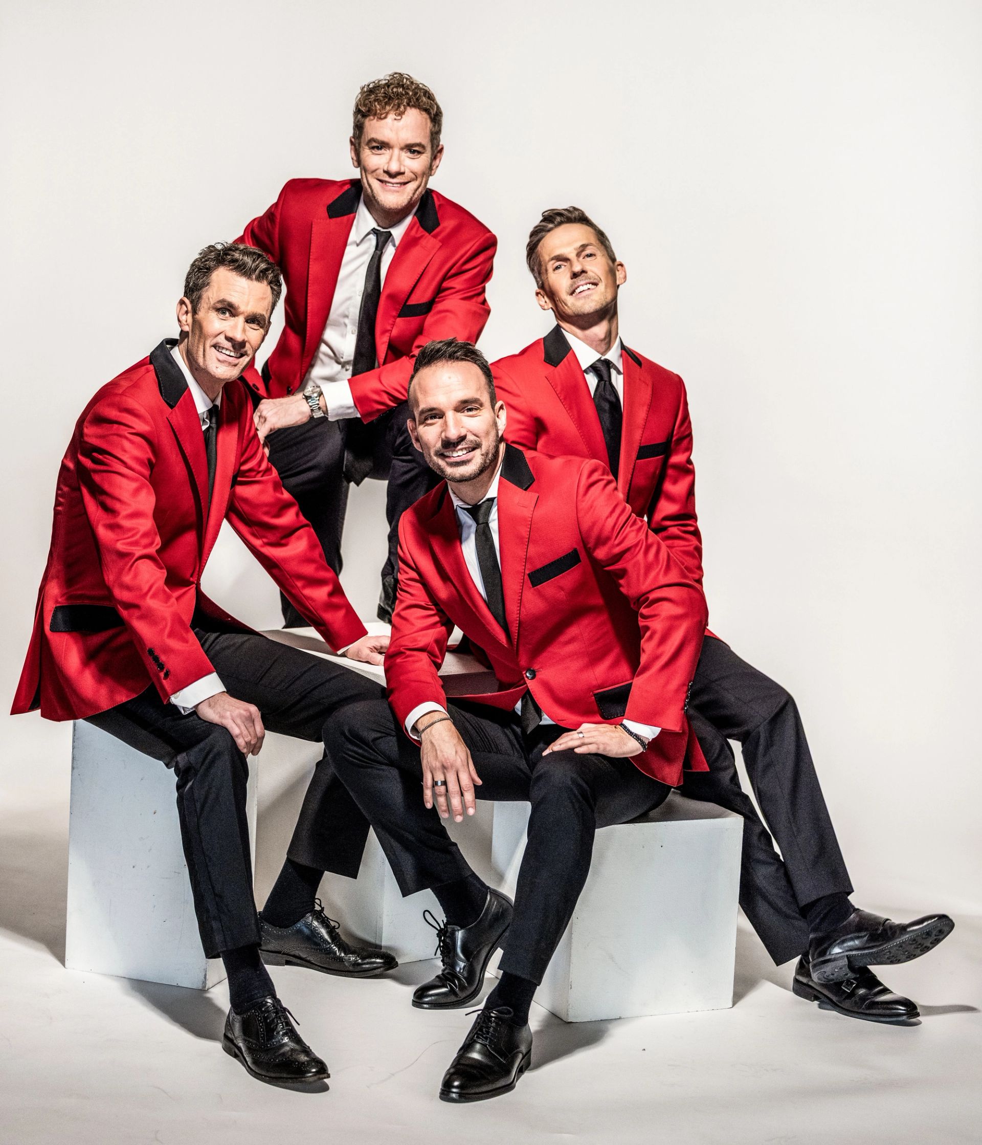 Pressbild för Oh What a Night. Peter Johansson, Bruno Mitsogiannis, David Lindgren och Robert Rydberg har på sig röda kavajer och svart kostym byxor. De tittar in i kameran och ler.