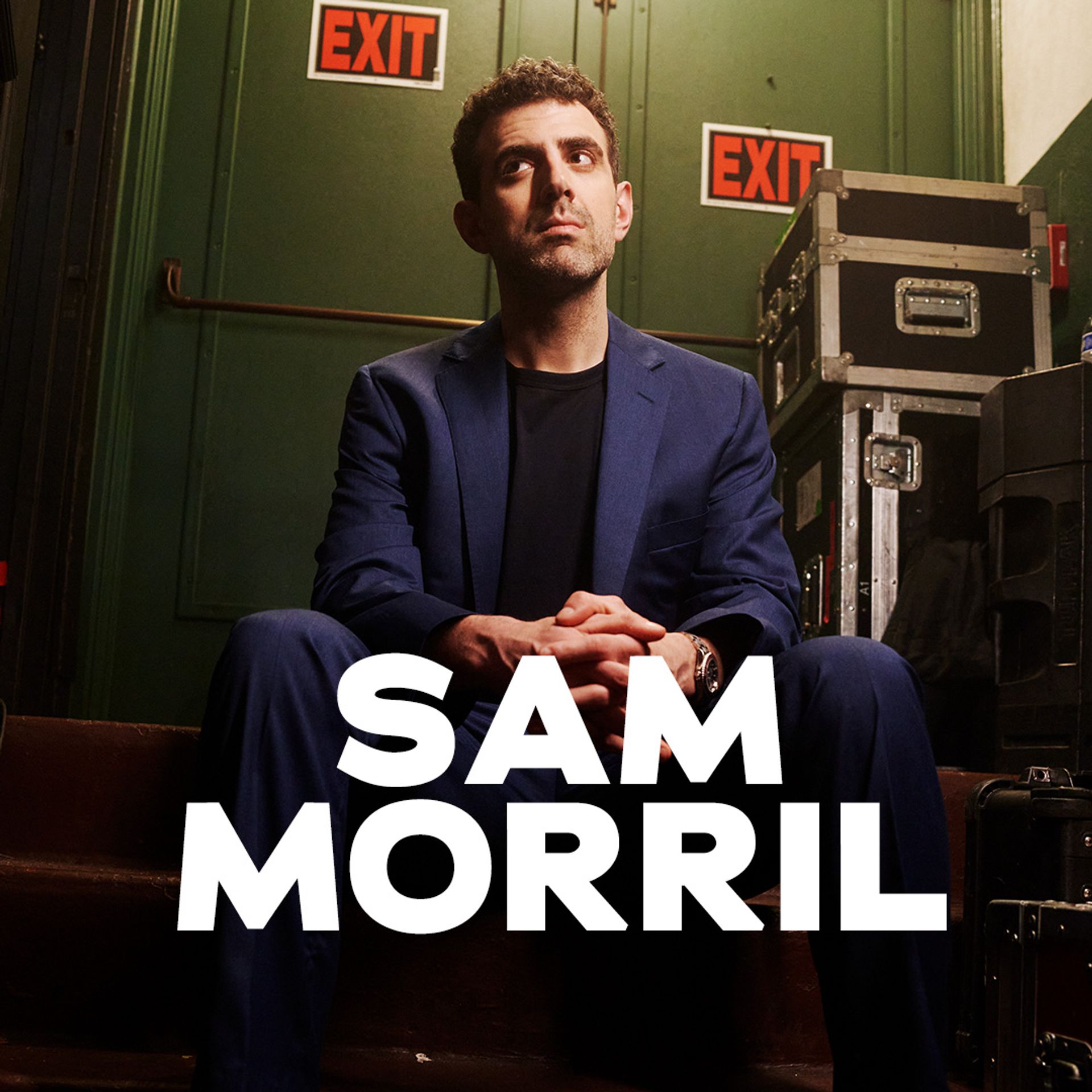 Sam Morril standup show – komiker i blå kostym bakom scen med EXIT-skyltar, porträtt inför liveföreställning