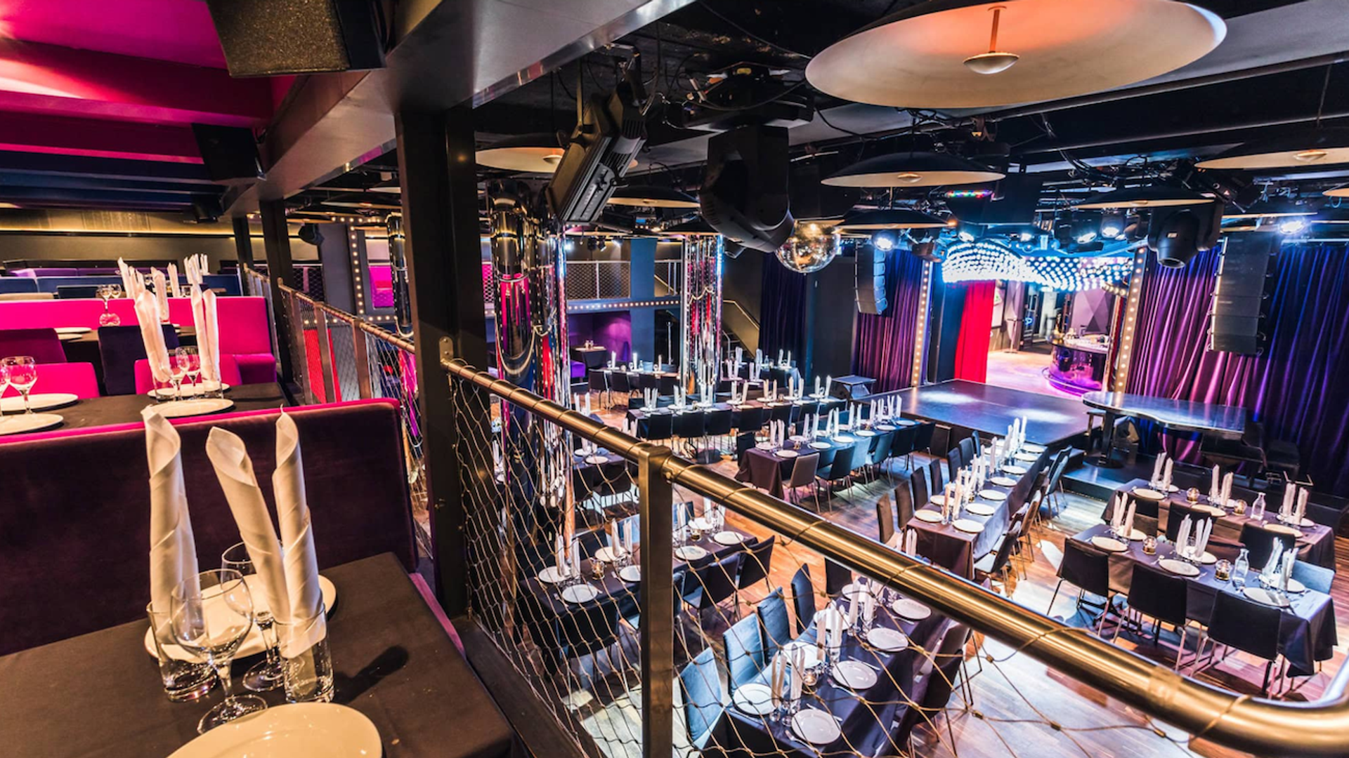 Interiör av Wallmans Stockholm med dukade middagsbord, scen med ridåer och färgglad belysning, redo för dinner show.