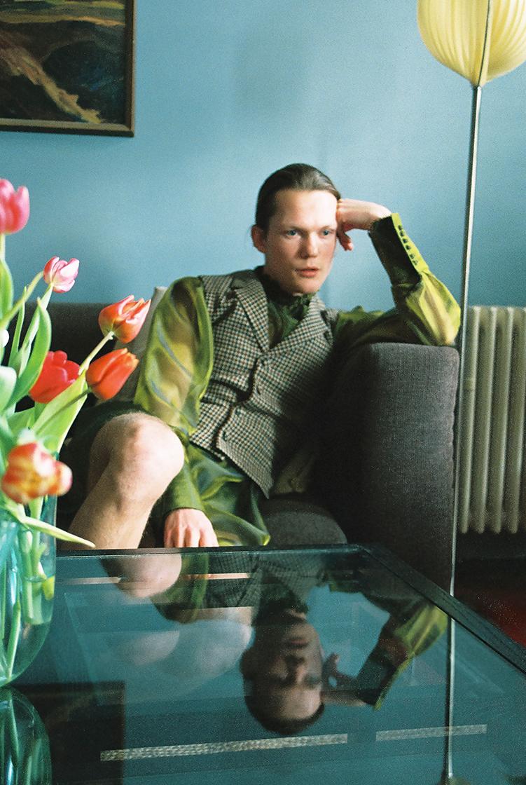 male model sits on couch next to flowers