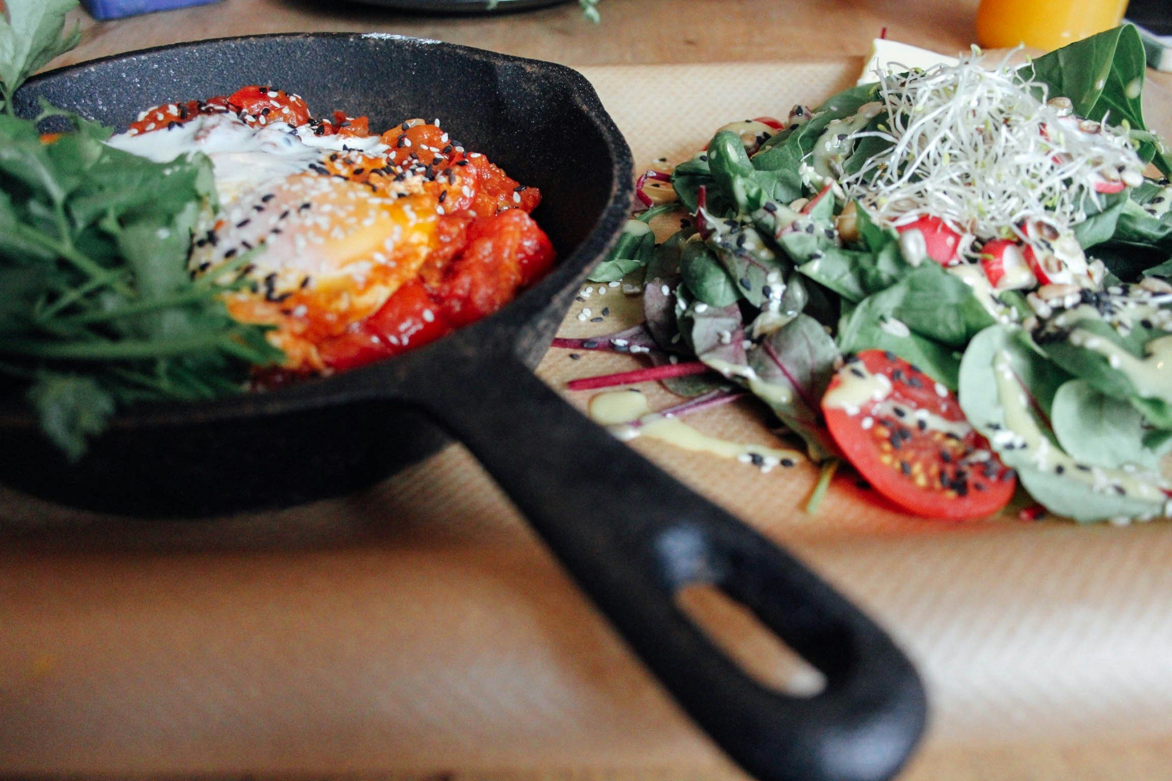 A cast iron skillet with eggs and vegetables next to a fresh salad