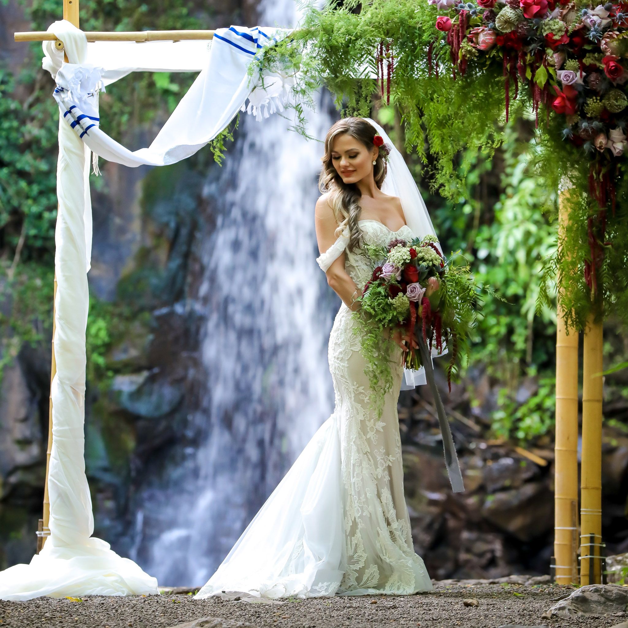 Bride beneath a floral wedding canopy with a waterfall at South Shore Gardens on Kauaʻi