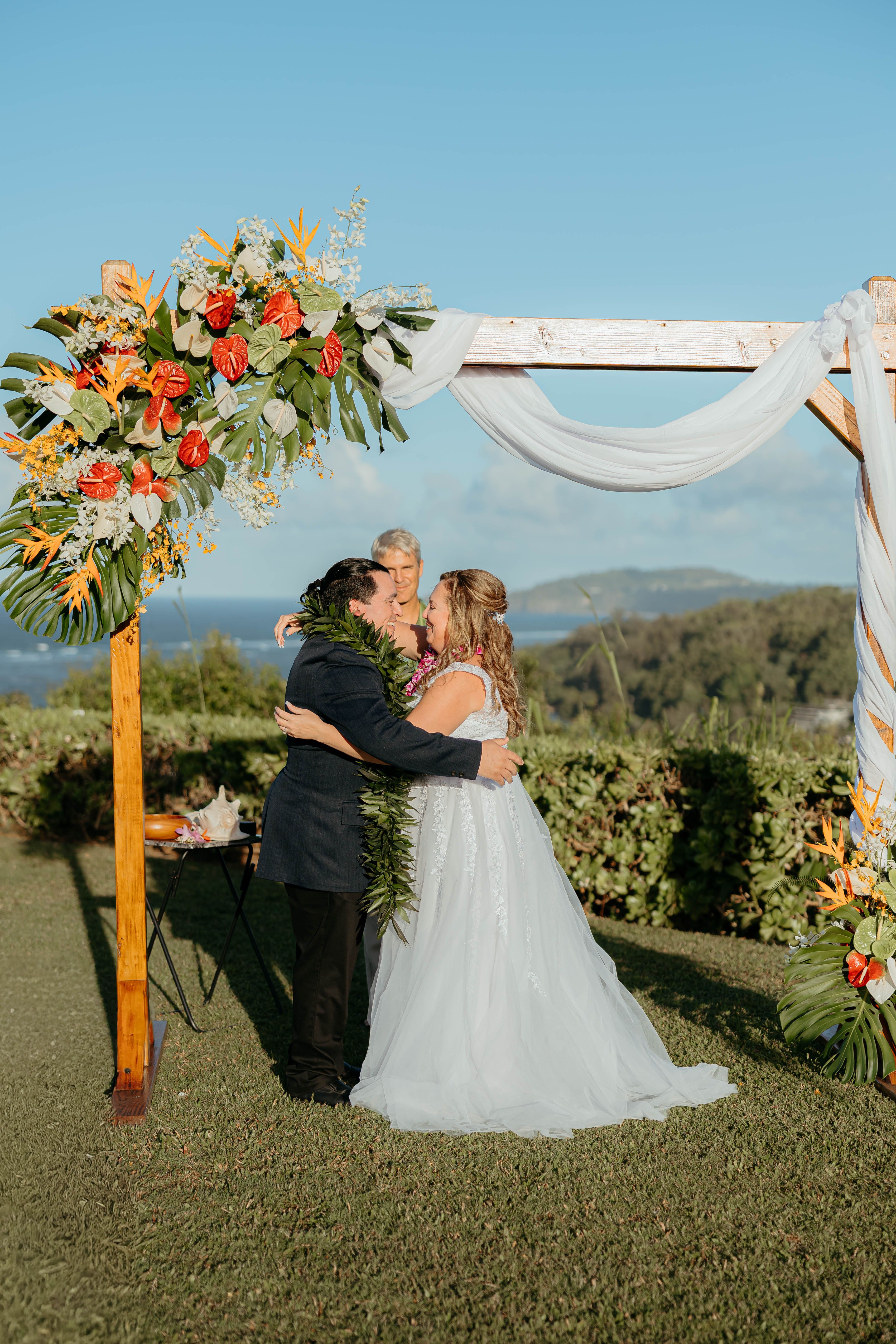 Jennifer and Mark at their Kauaʻi wedding under a tropical arch, Embrace of Aloha