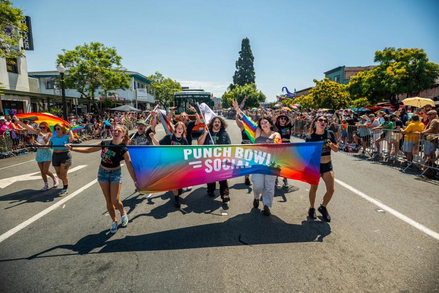 Punch Bowl Social staff and guests marching with a rainbow banner at a Pride parade