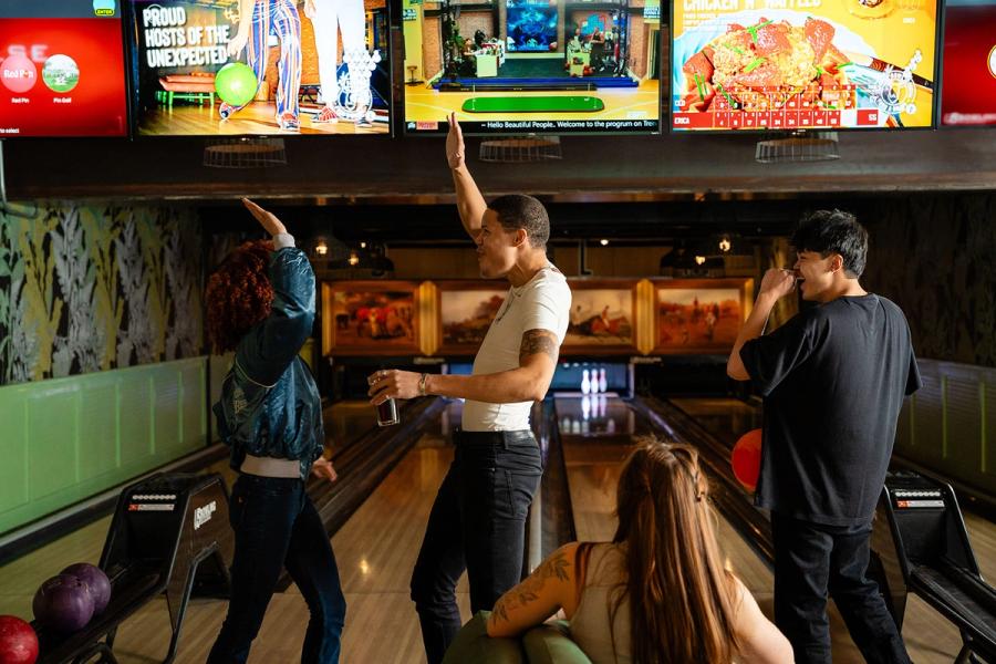 Friends bowling and celebrating under retro screens at Punch Bowl Social