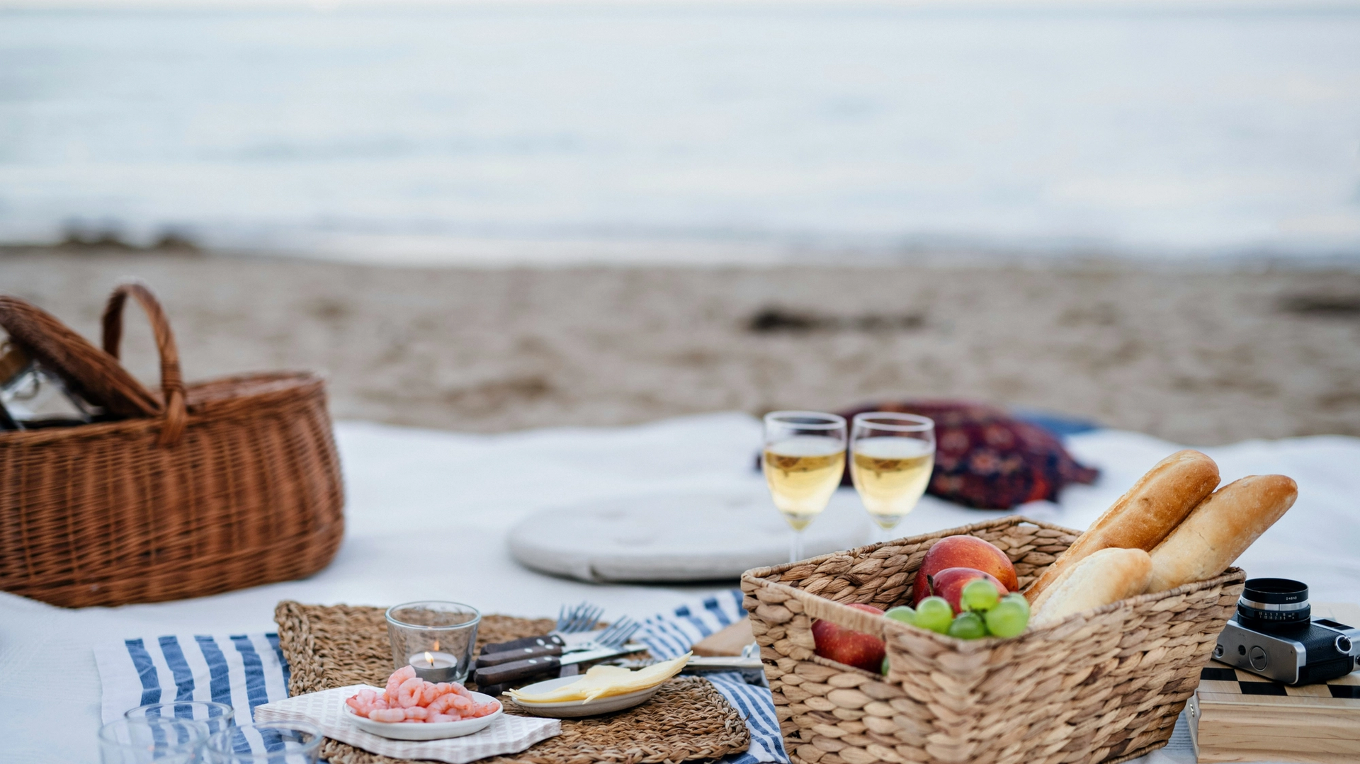 Image of a picnic basked with bread and food with wine by the ocean