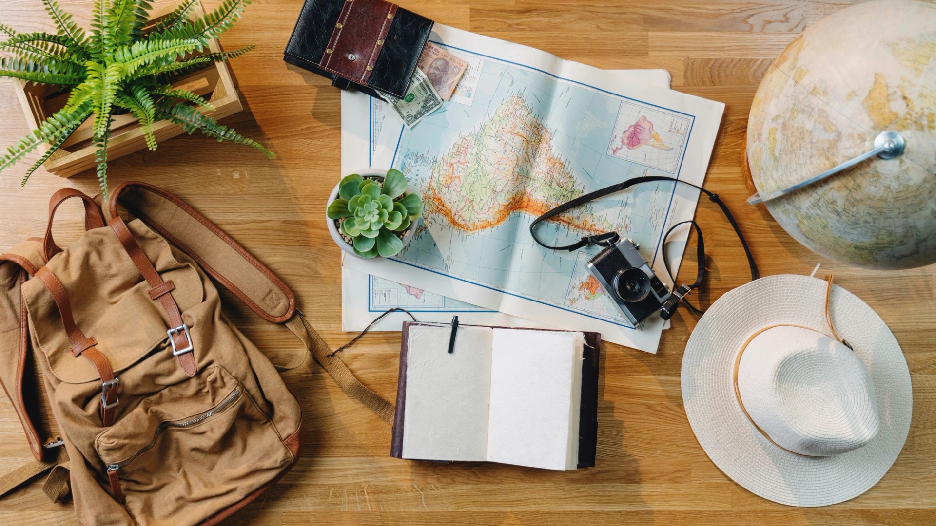 Image of a desk view with maps, a camera, travel equipment, and a globe