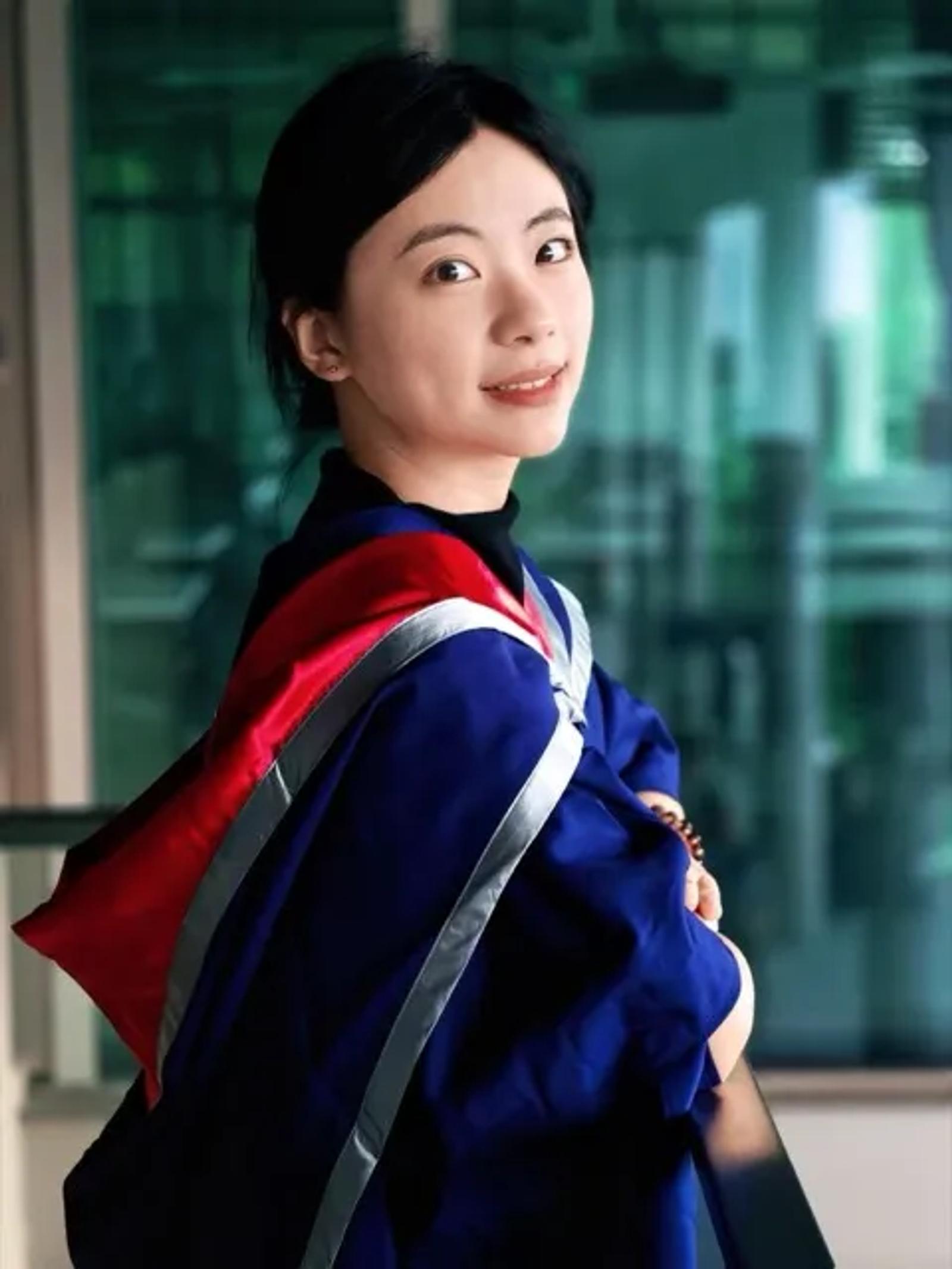 Xinyi He in a graduation gown, looking over her shoulder toward the camera