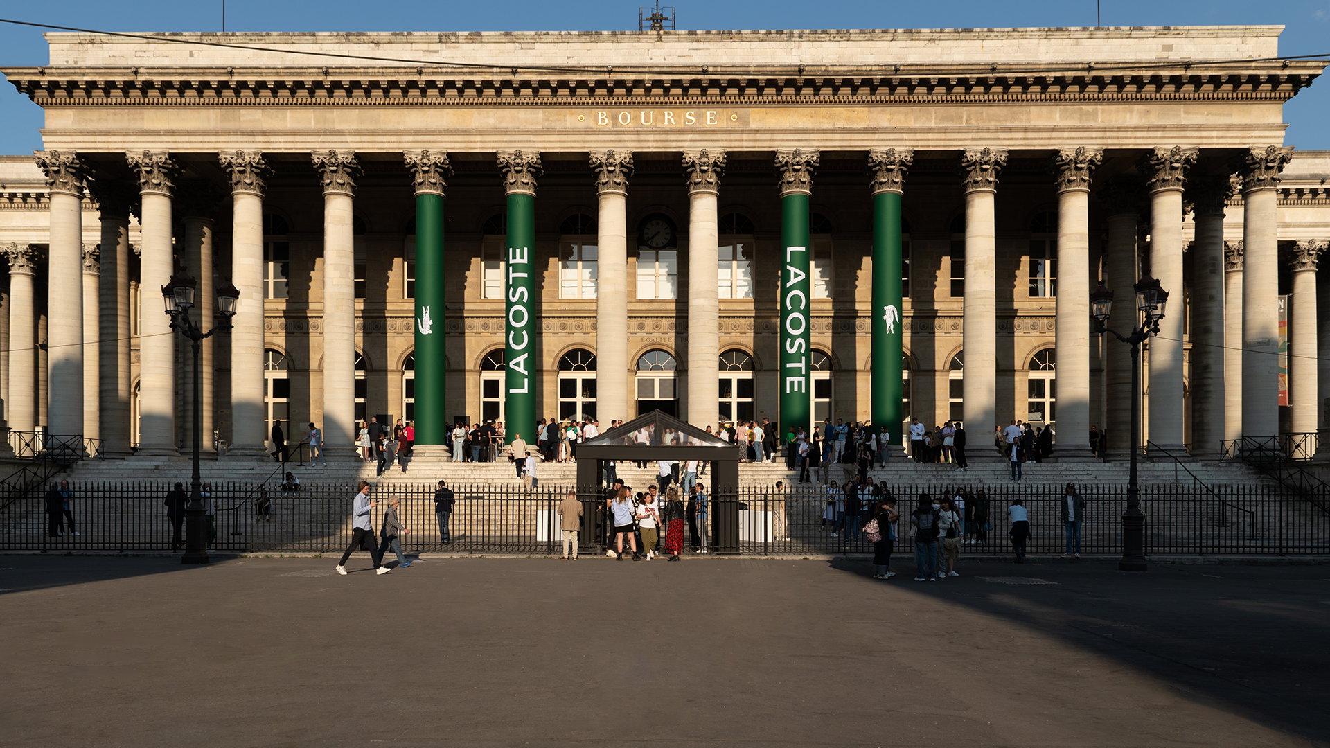 Facade of Palais Brongniart in Paris, branded with Lacoste logo on green columns for the runway show.