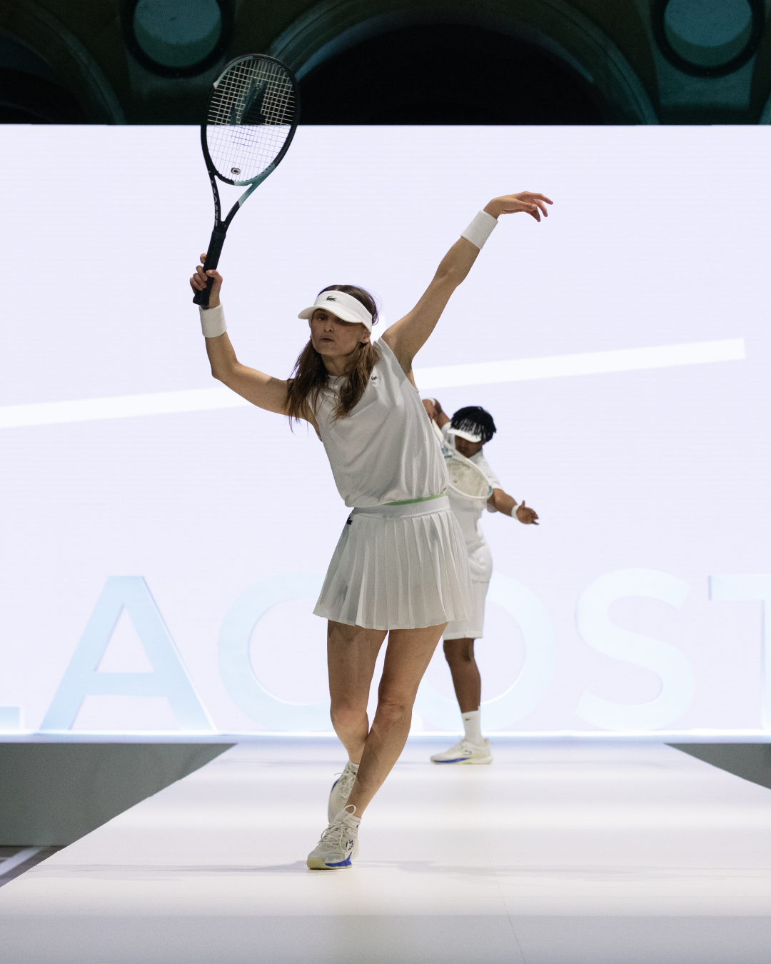 Two models dancing on the runway at Palais Brongniart in Paris in Lacoste white outfits.