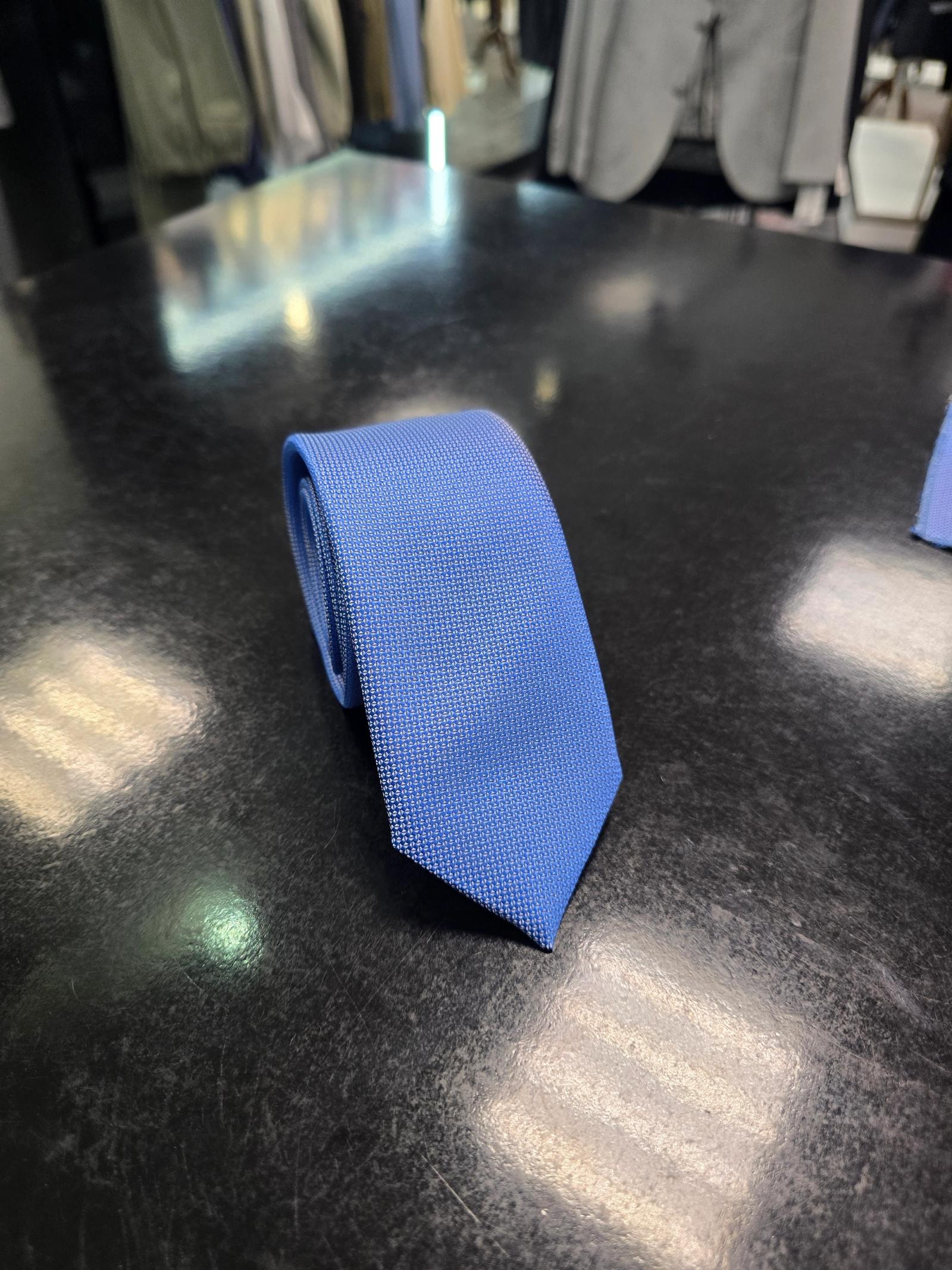 Viento textured cornflower blue tie, rolled view on dark counter