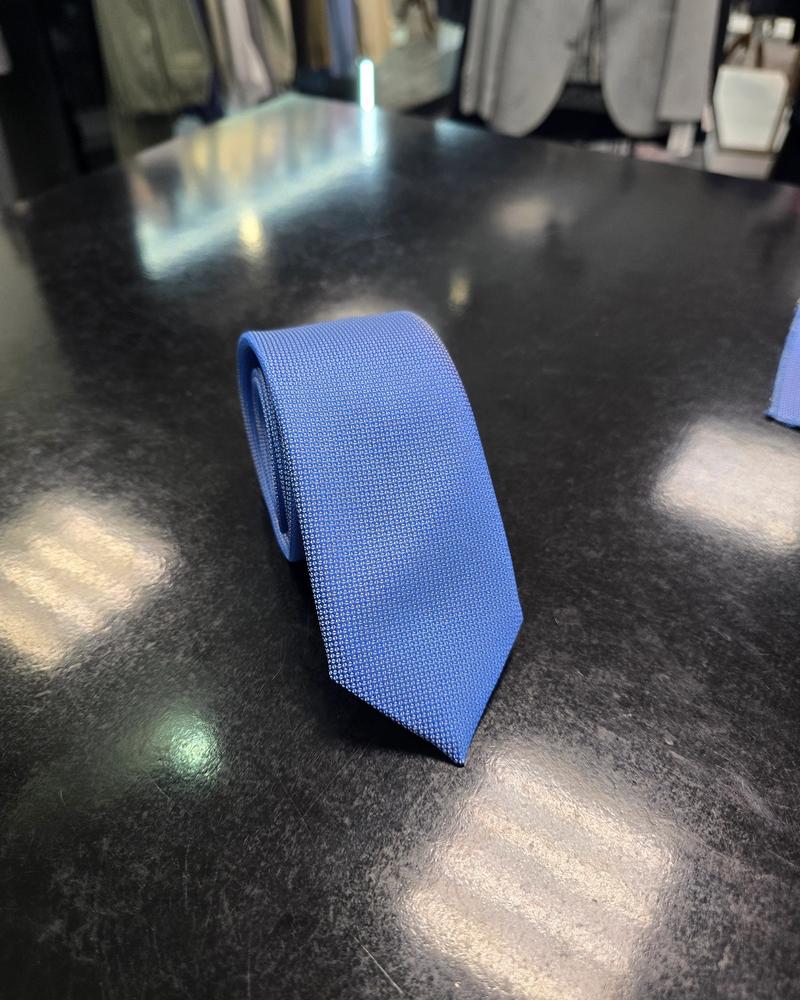 Viento textured cornflower blue tie, rolled view on dark counter