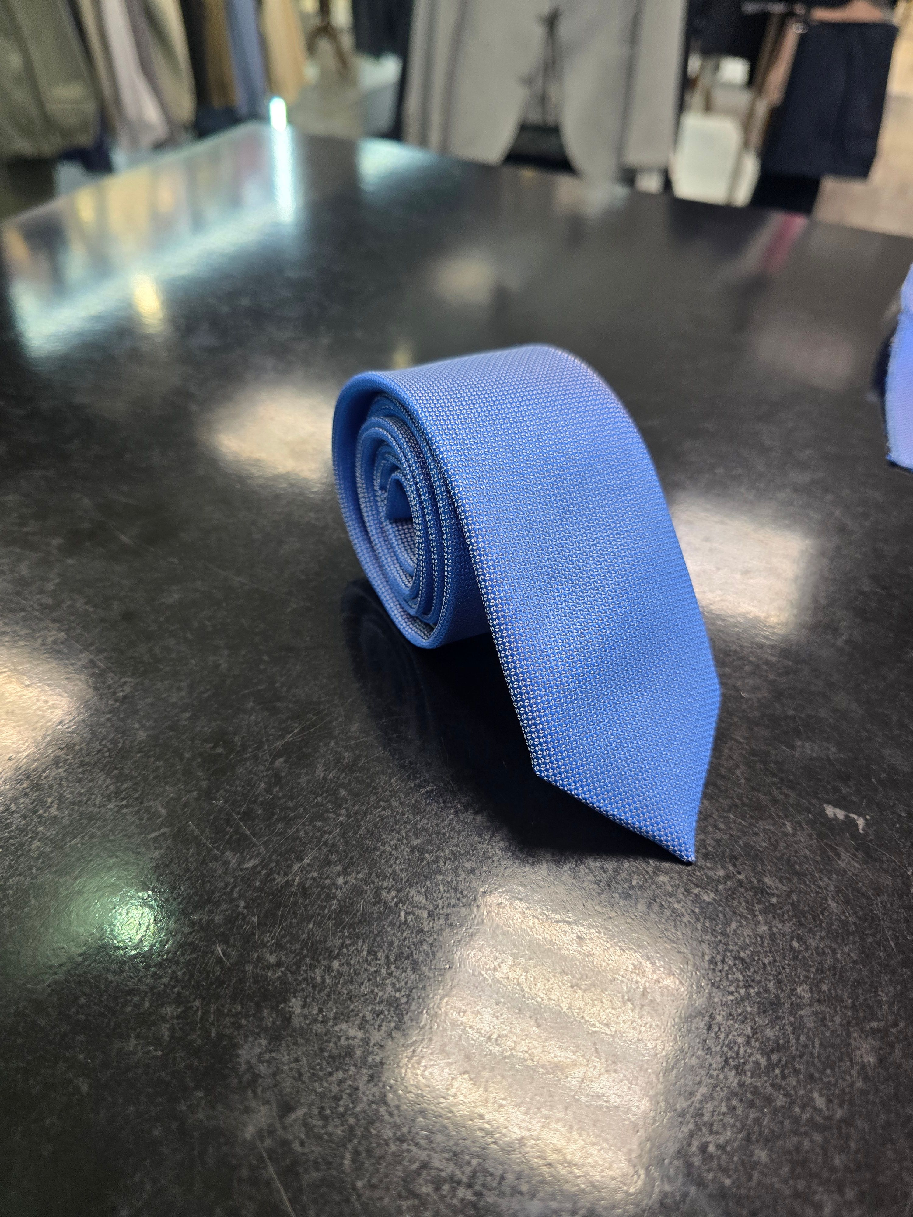 Viento textured cornflower blue tie, vertical full-length view on dark counter