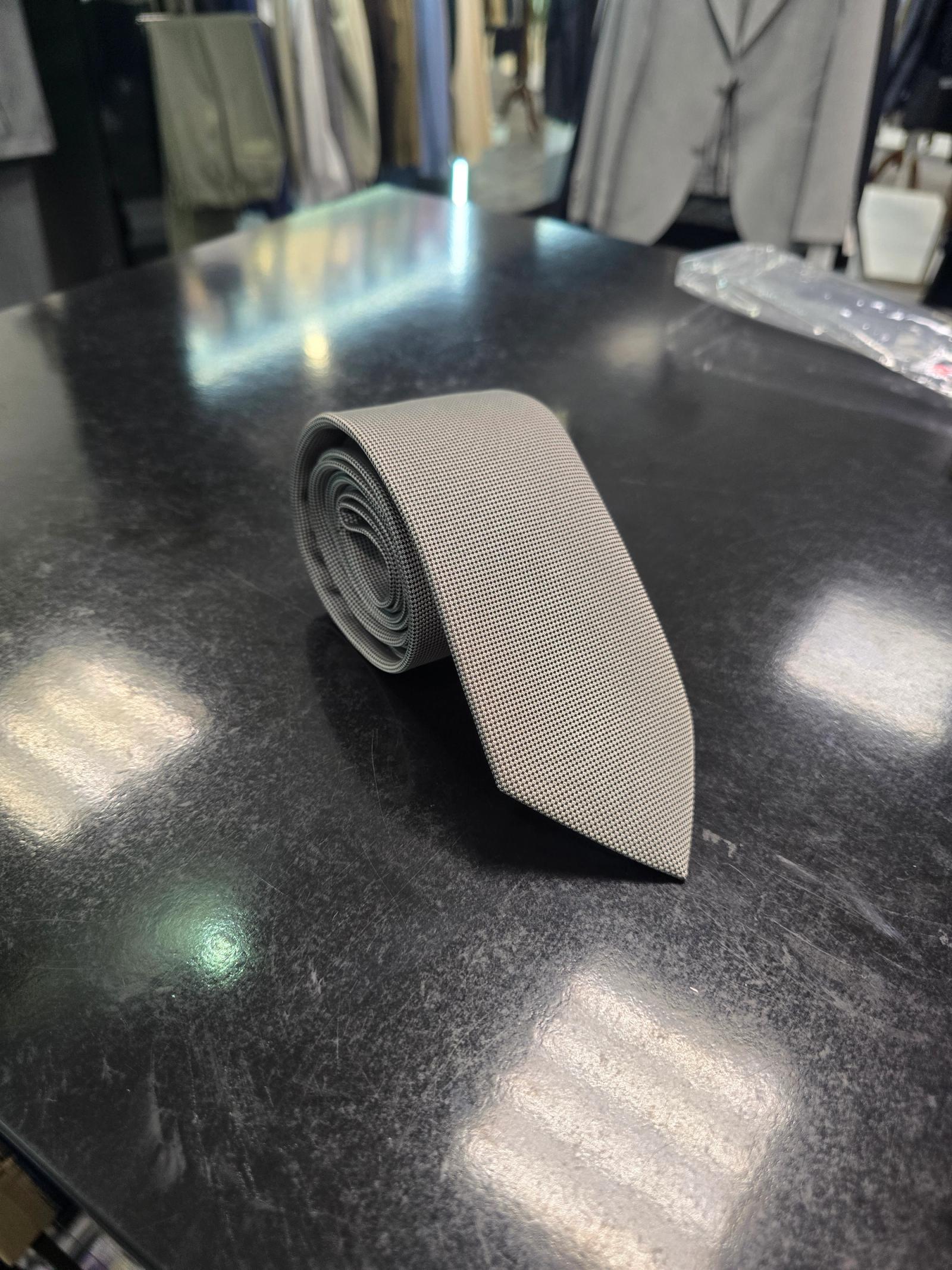 Grey textured men's tie neatly rolled on a dark surface in a menswear store setting.