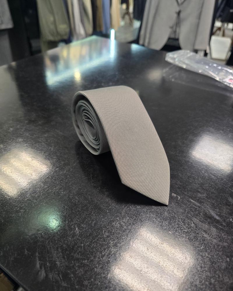 Grey textured men's tie neatly rolled on a dark surface in a menswear store setting.
