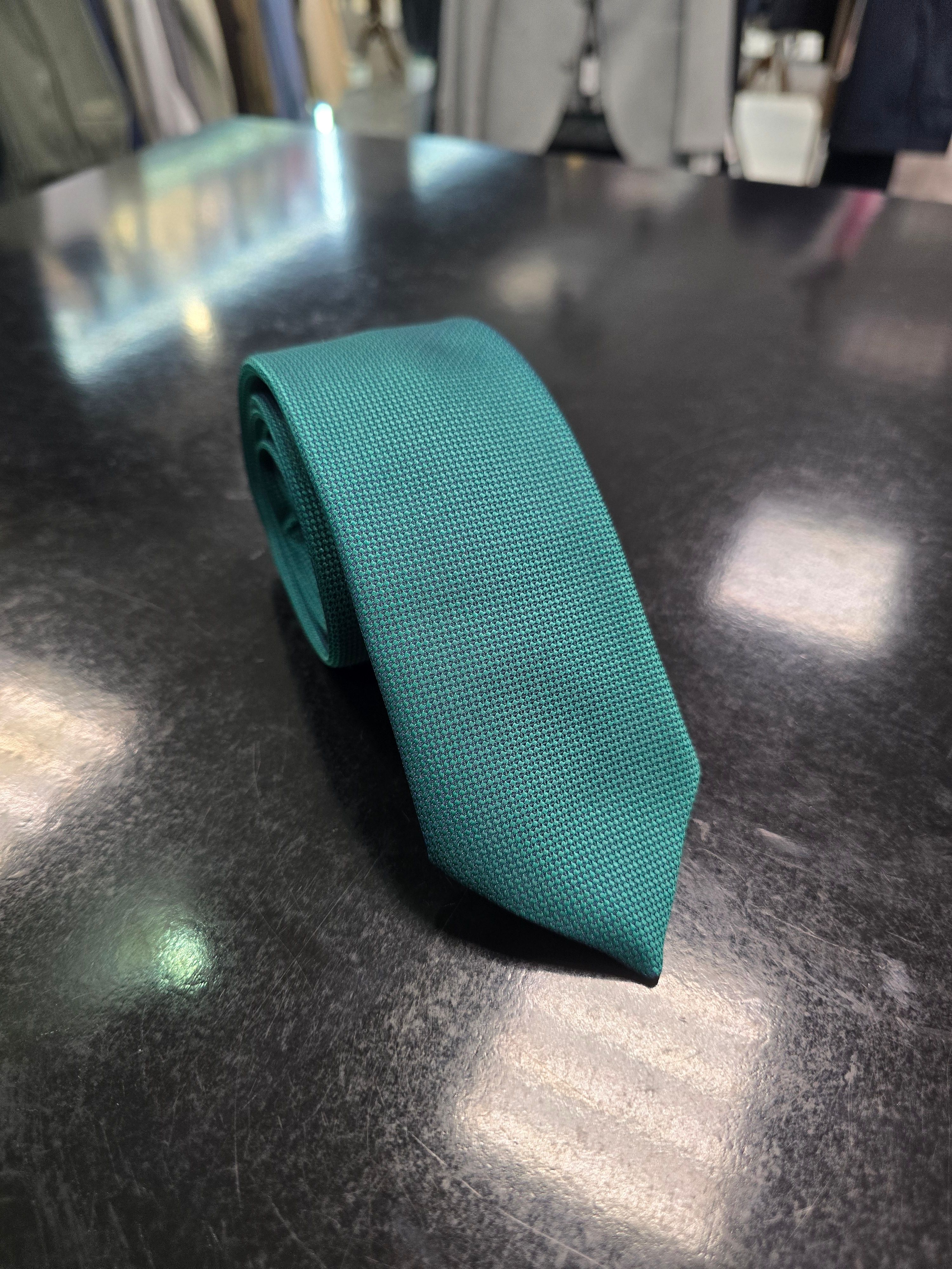Viento textured teal green tie, rolled view on dark counter