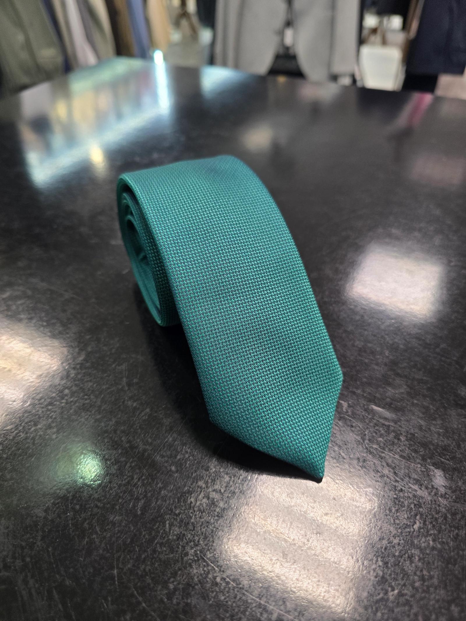 Viento textured teal green tie, rolled view on dark counter