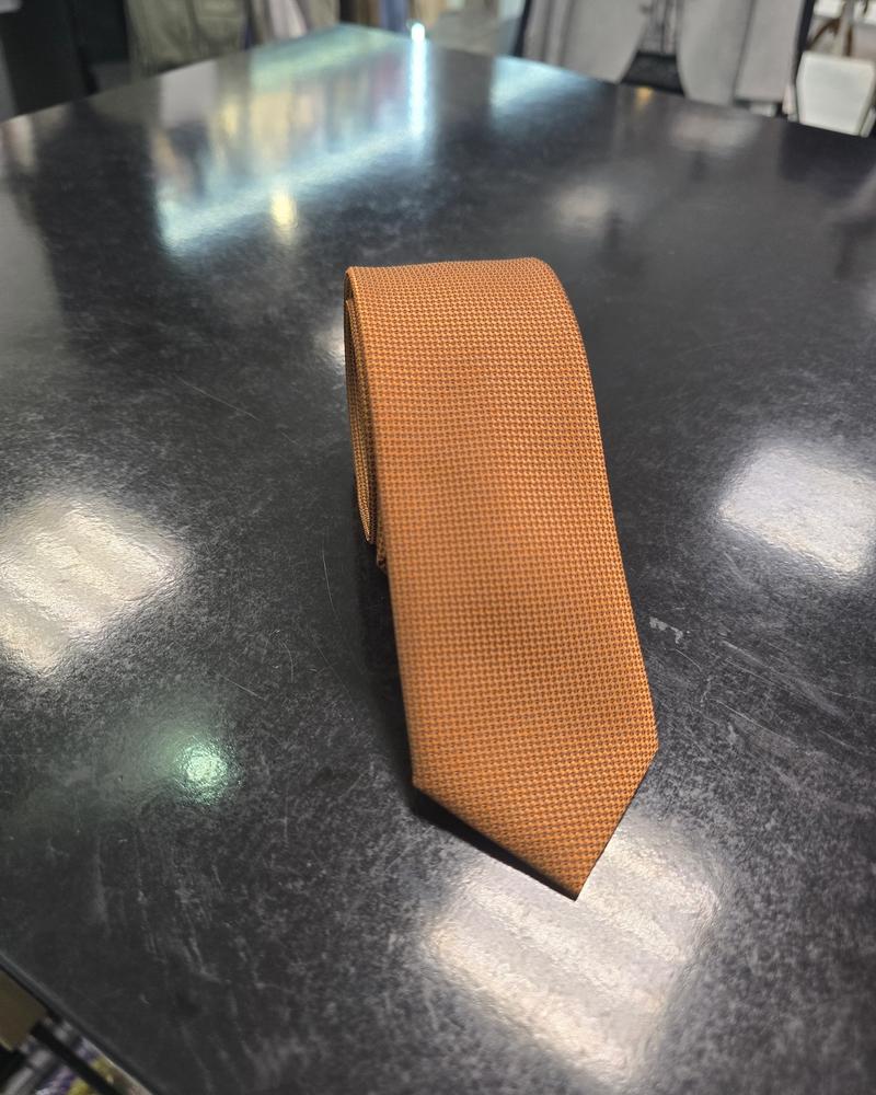 Viento textured burnt orange tie, rolled view on dark counter