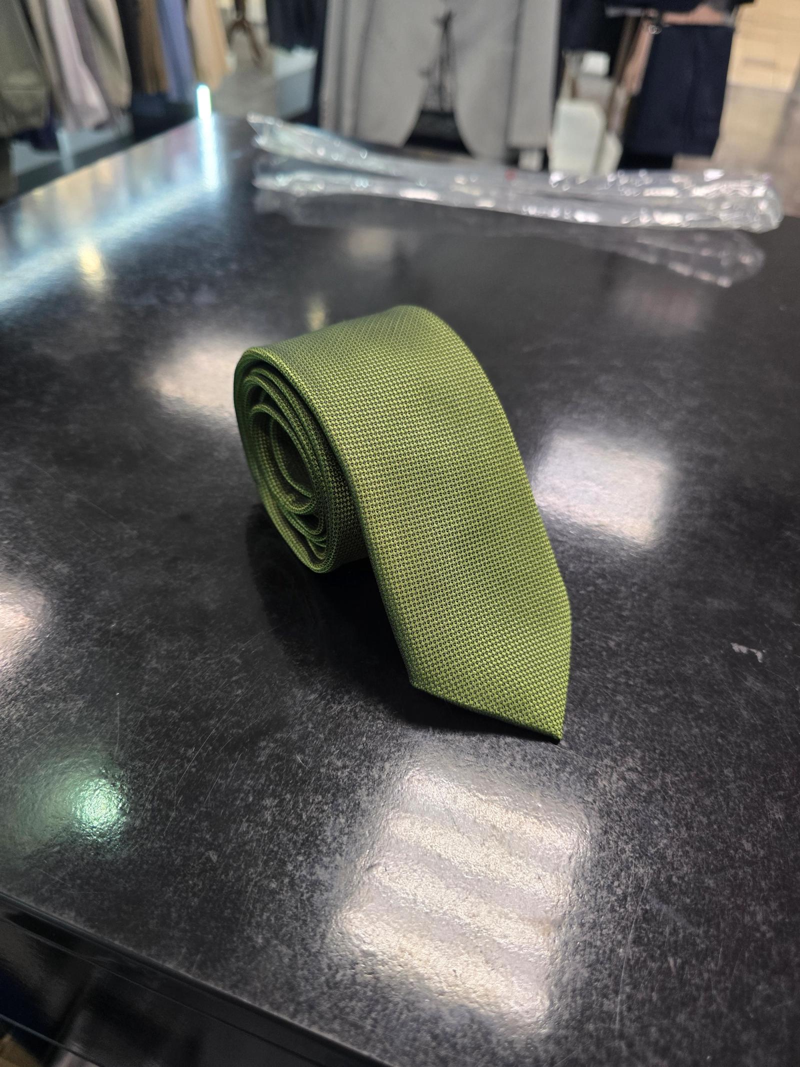 Olive green textured men's tie displayed flat on a dark surface in a menswear store.