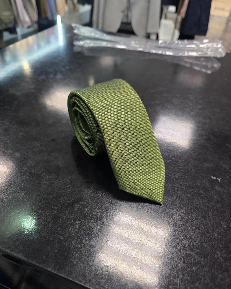 Olive green textured men's tie displayed flat on a dark surface in a menswear store.