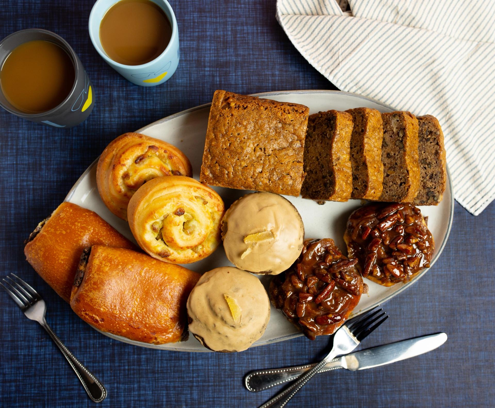 Plate of Sticky buns, Gingerbread Muffins, Chocolate Brioches, Pain Aux Raisin and Banana Bread and two cup of coffee on the side
