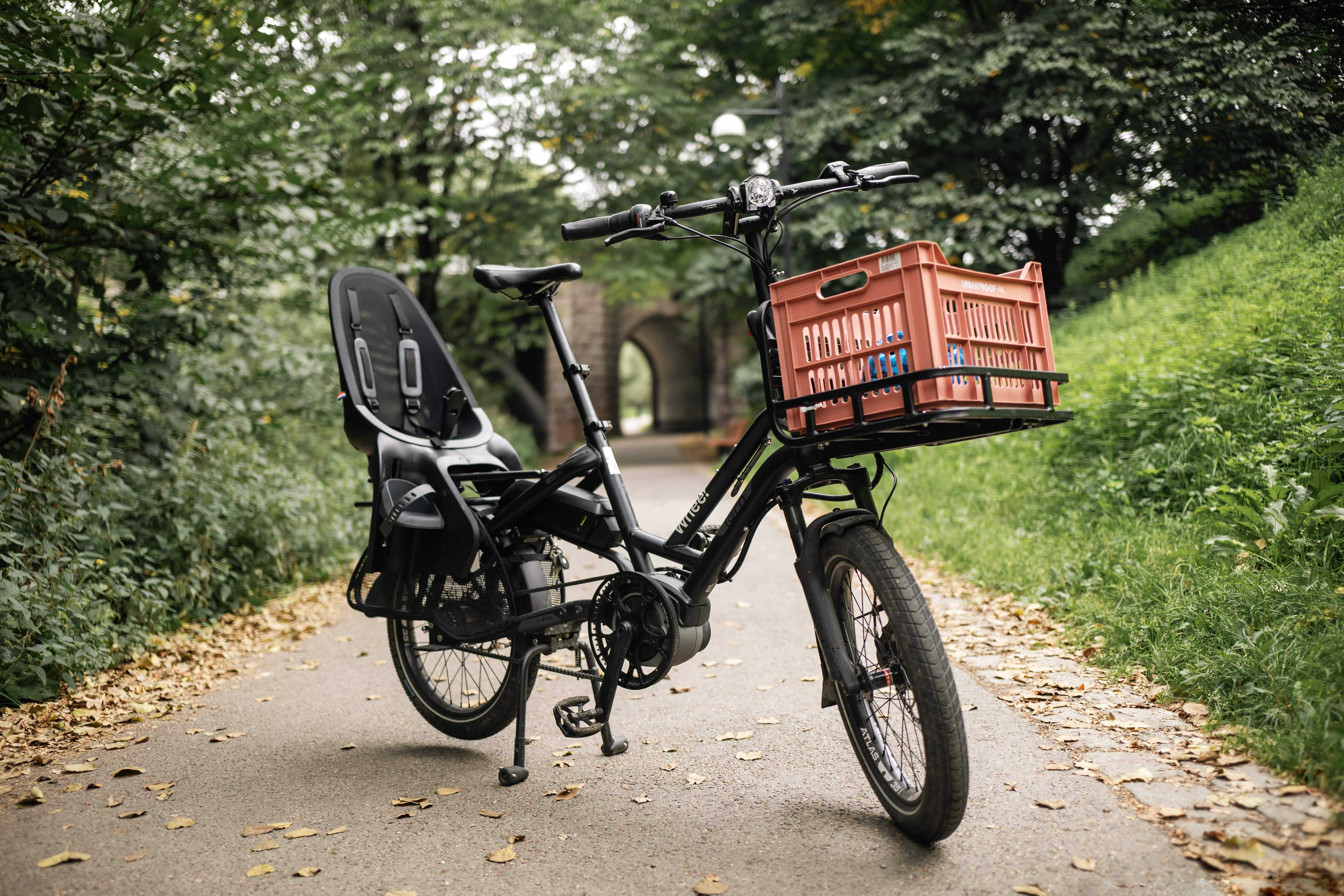 En Whee!-sykkel parkert på en gangvei. Sykkelen har frontbærer og montert barnesete.