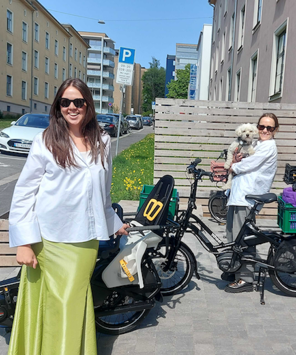 Karoline Kjønniksen og Ingrid Vik Lysne fra Fæbrik står utenfor Whee! Sandaker med sine nye Whee!-sykler. Ingrid Vik Lysne holder en hund. 