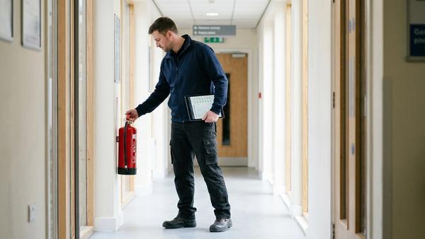 Technicien prestataire en sécurité incendie inspectant un extincteur mural avec un rapport de vérification