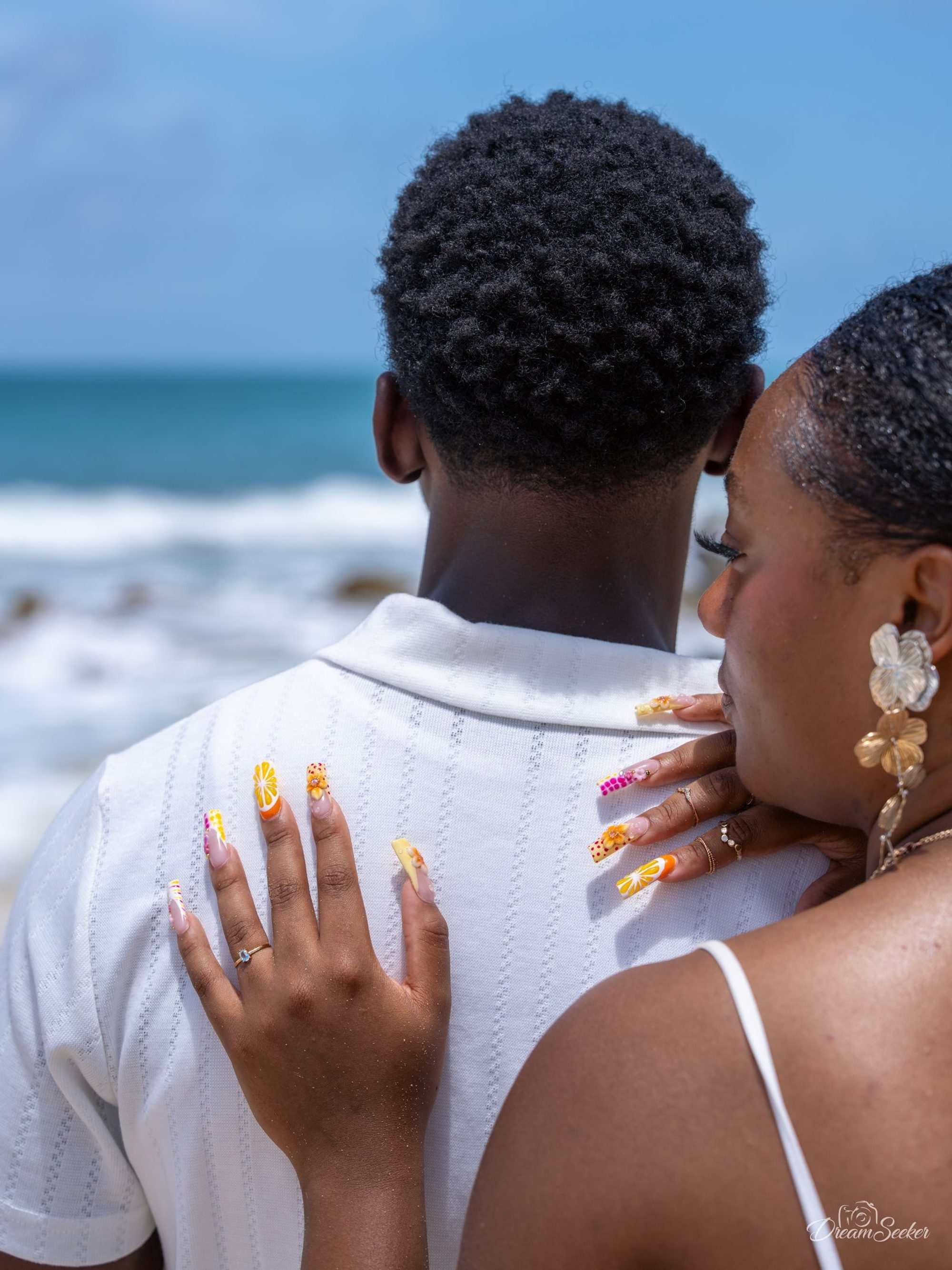 Couple de dos face à la mer, main de la femme sur l’épaule