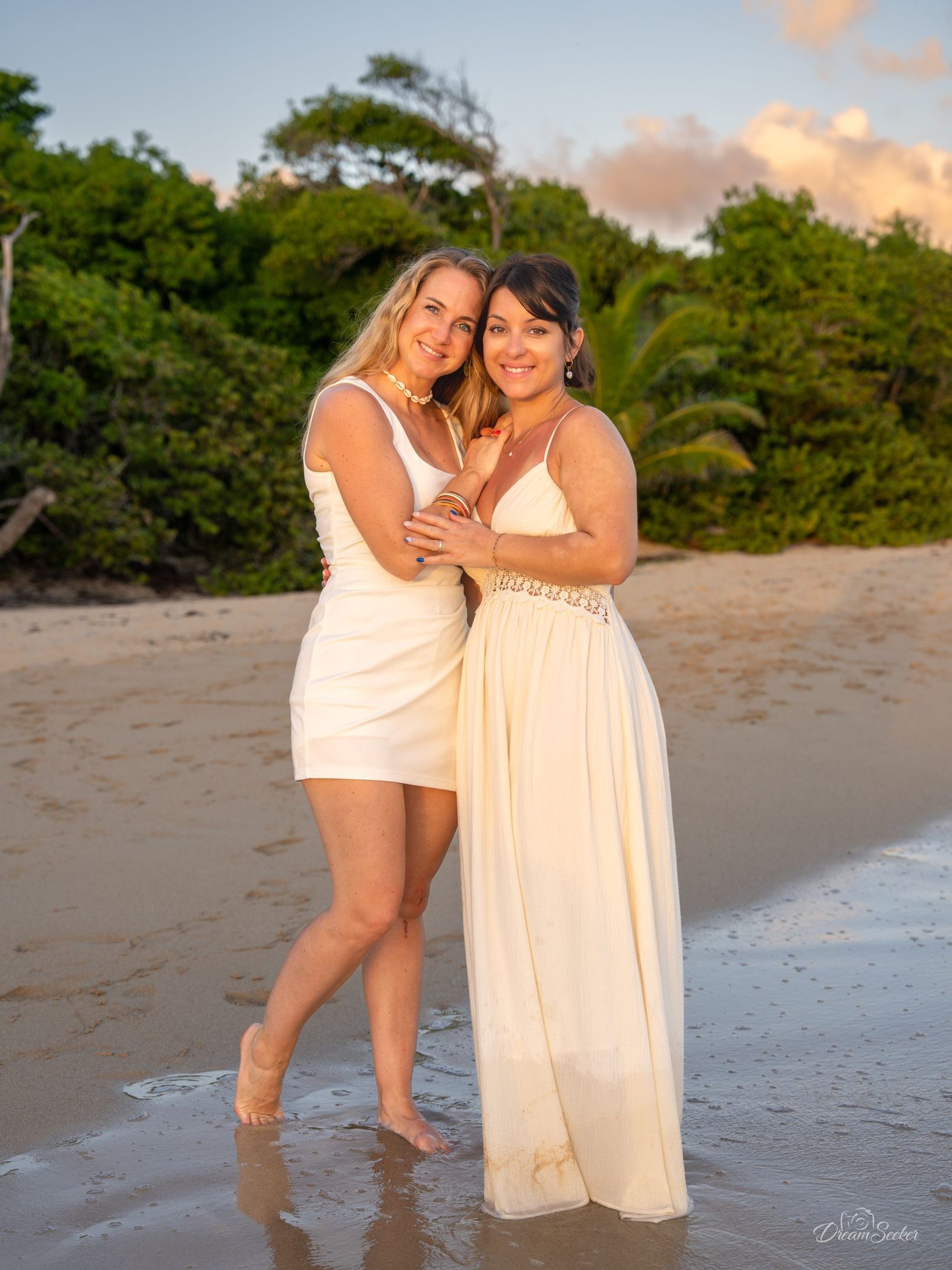 Deux femmes enlacées sur une plage, en blanc