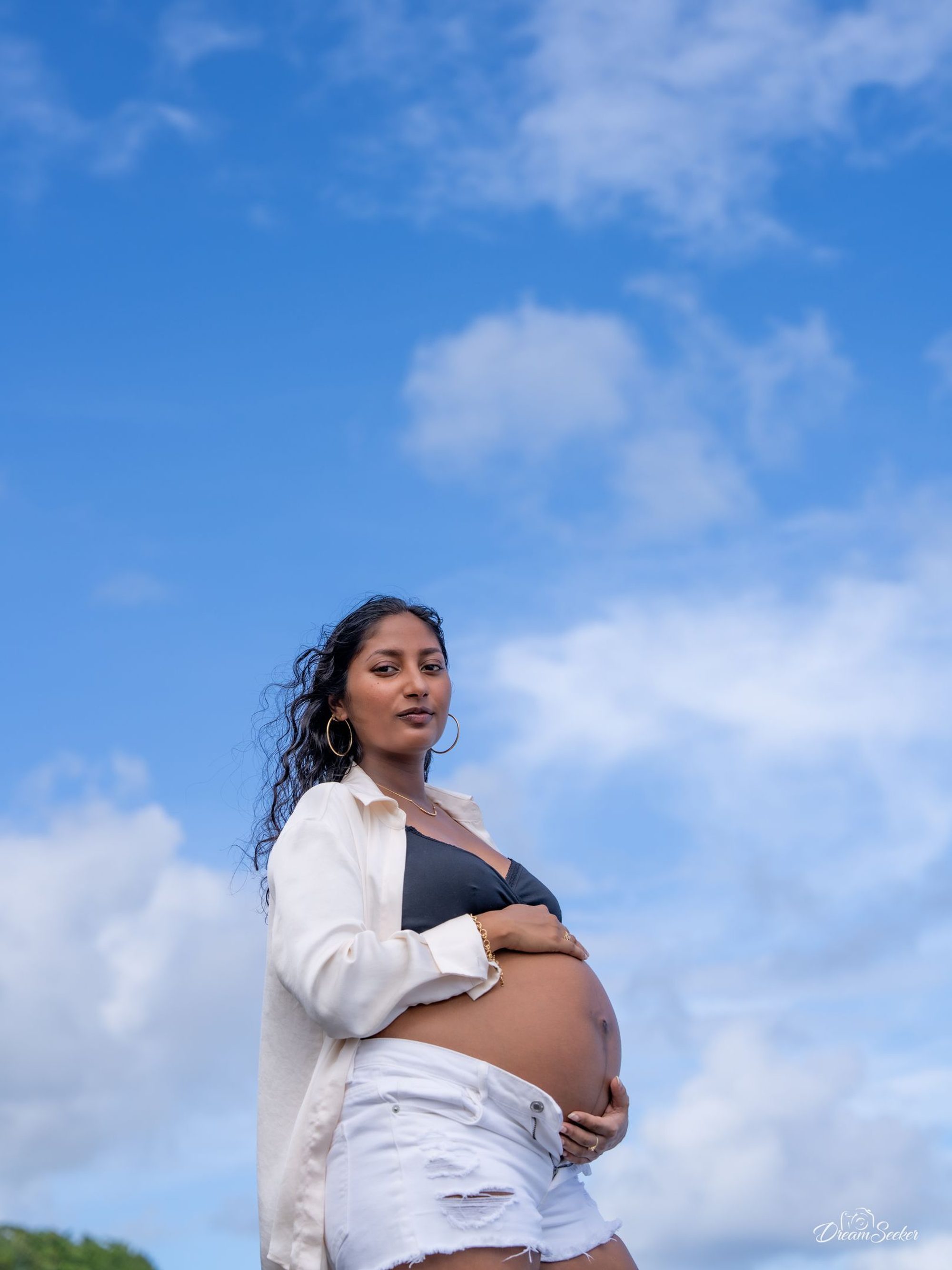 Future mère, main sur le ventre, sous un grand ciel bleu