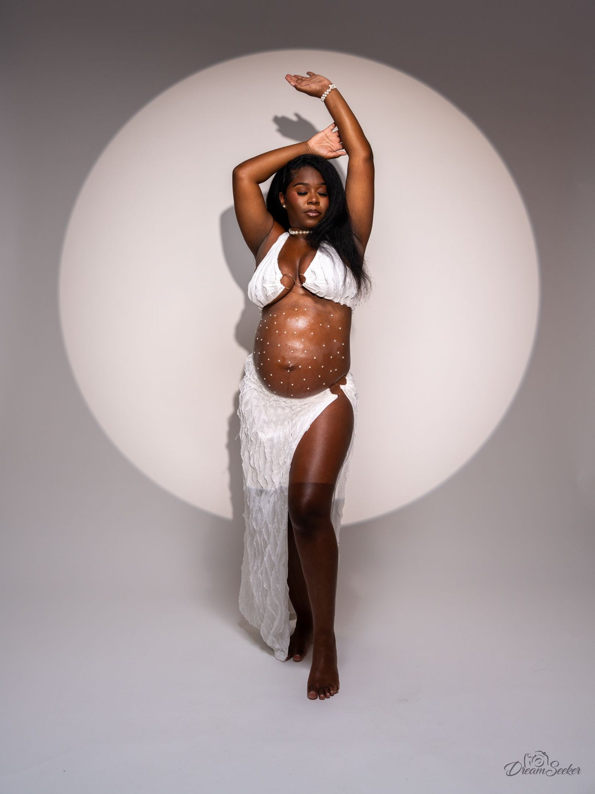 Future mère en blanc, bras levés devant un cercle de lumière