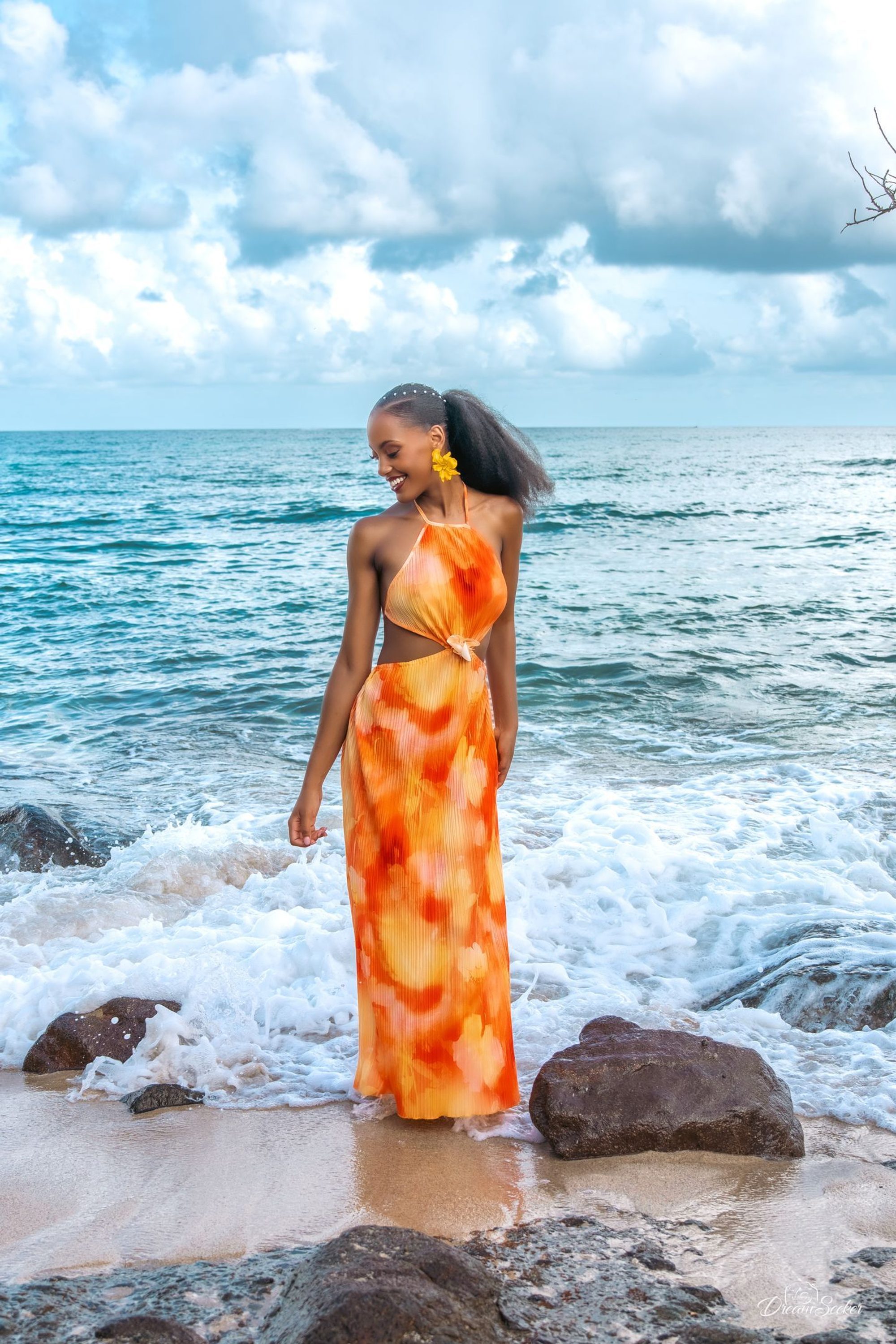 Femme en robe orange sur les rochers, vagues derrière