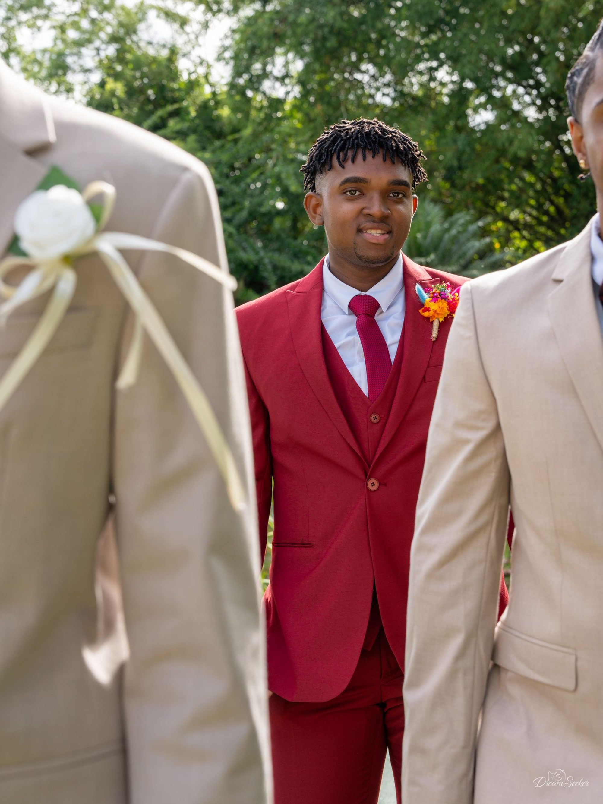 Jeune homme en costume rouge souriant entre deux invités