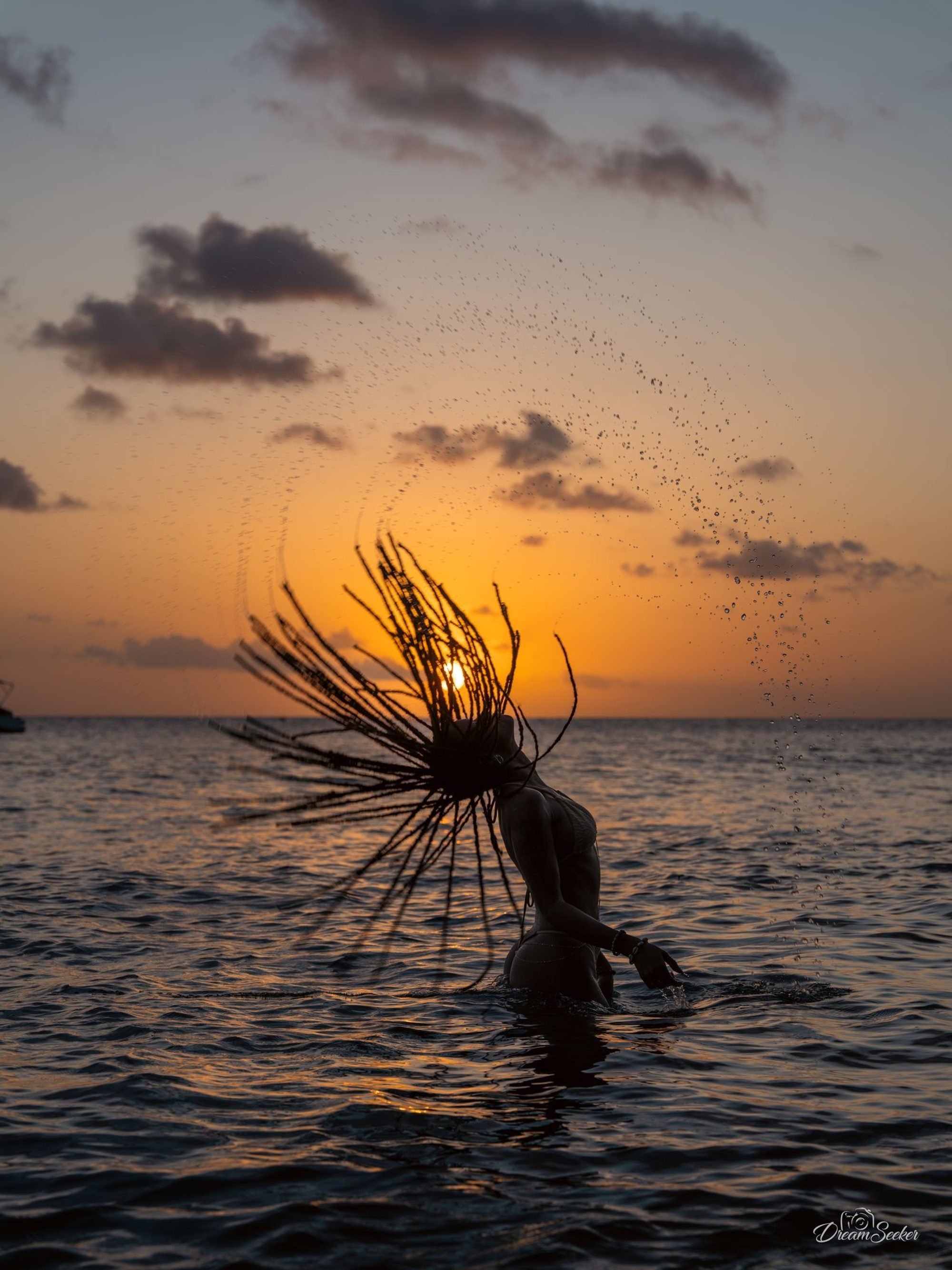 Silhouette lançant ses tresses hors de l’eau au coucher du soleil