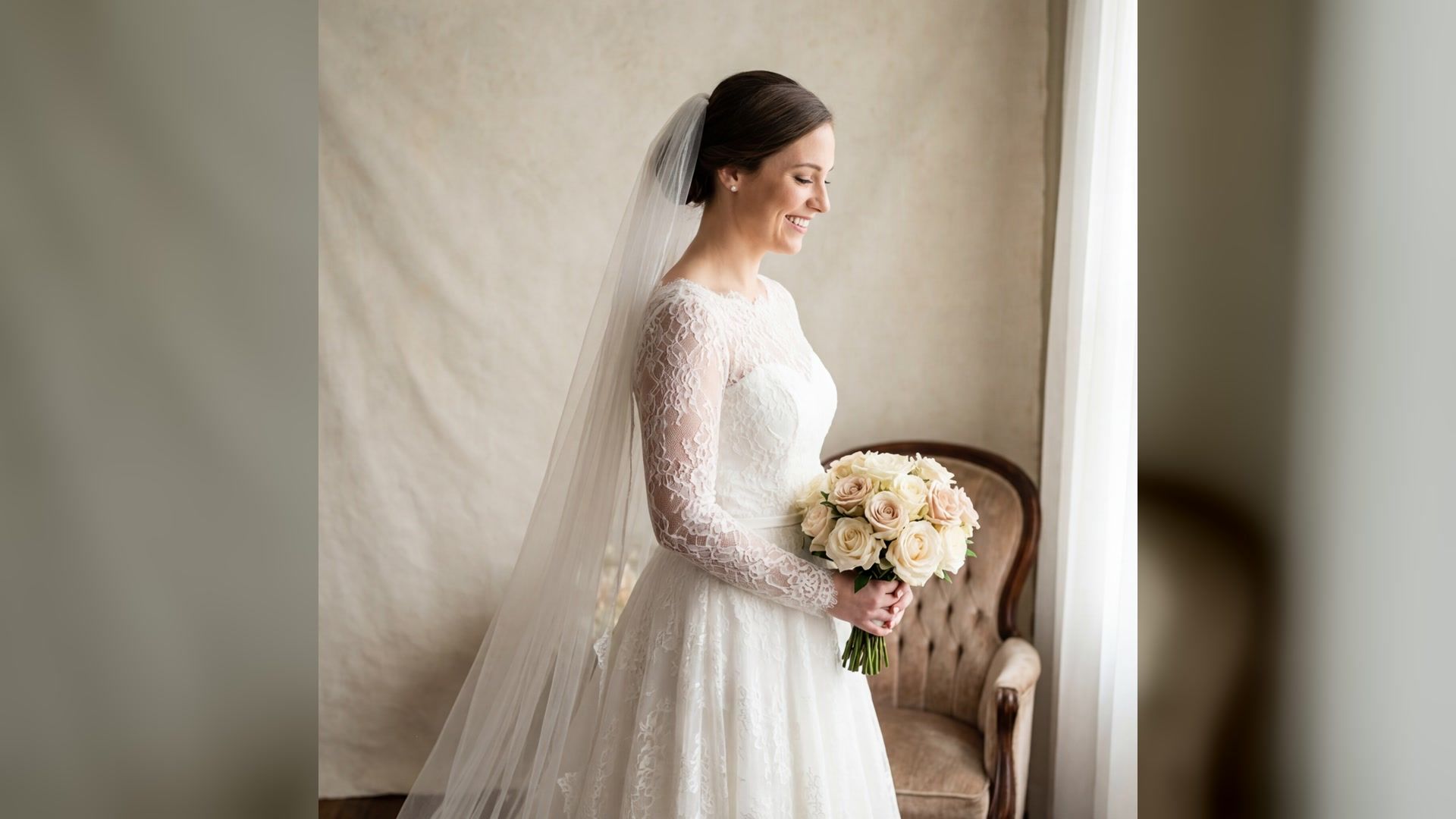 bride in a lace wedding dress and veil holding a pale rose bouquet beside a window