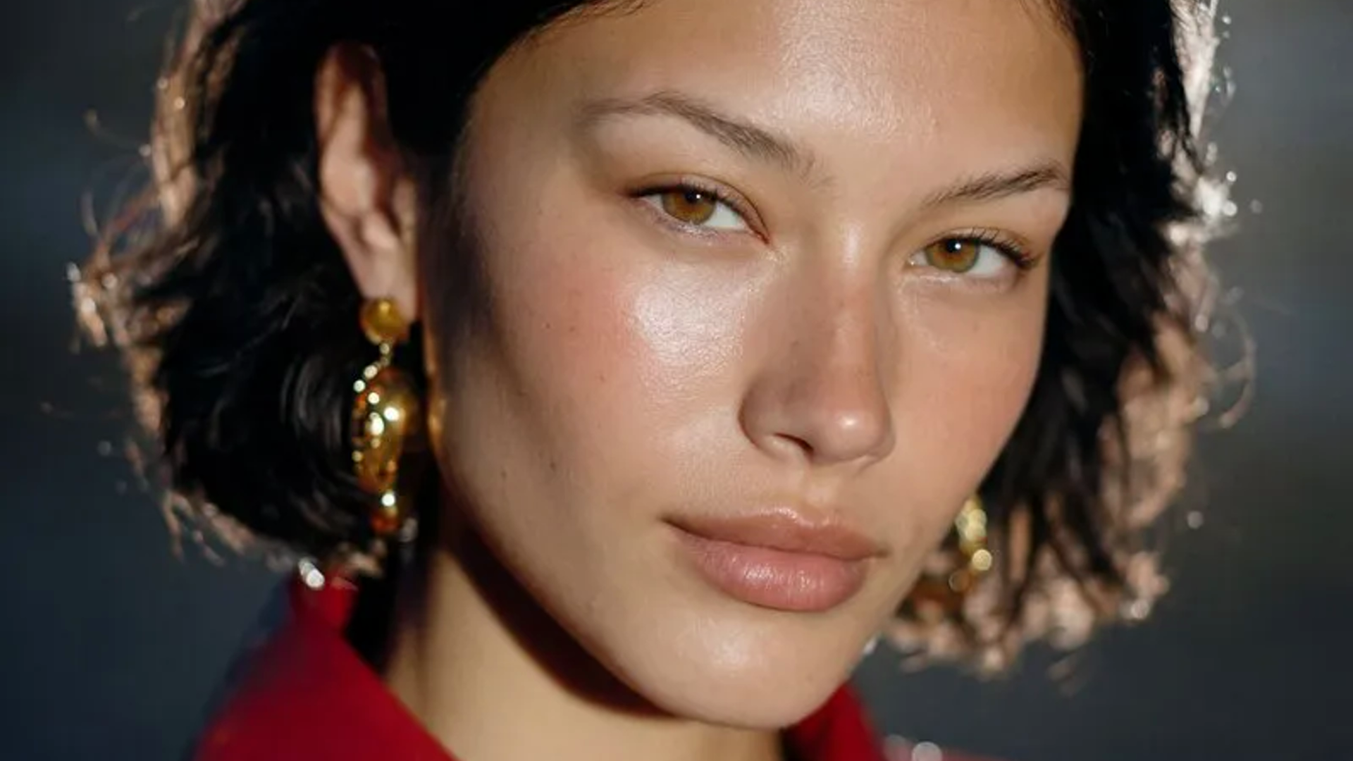 close portrait with dark hair, gold earrings, and clean studio lighting