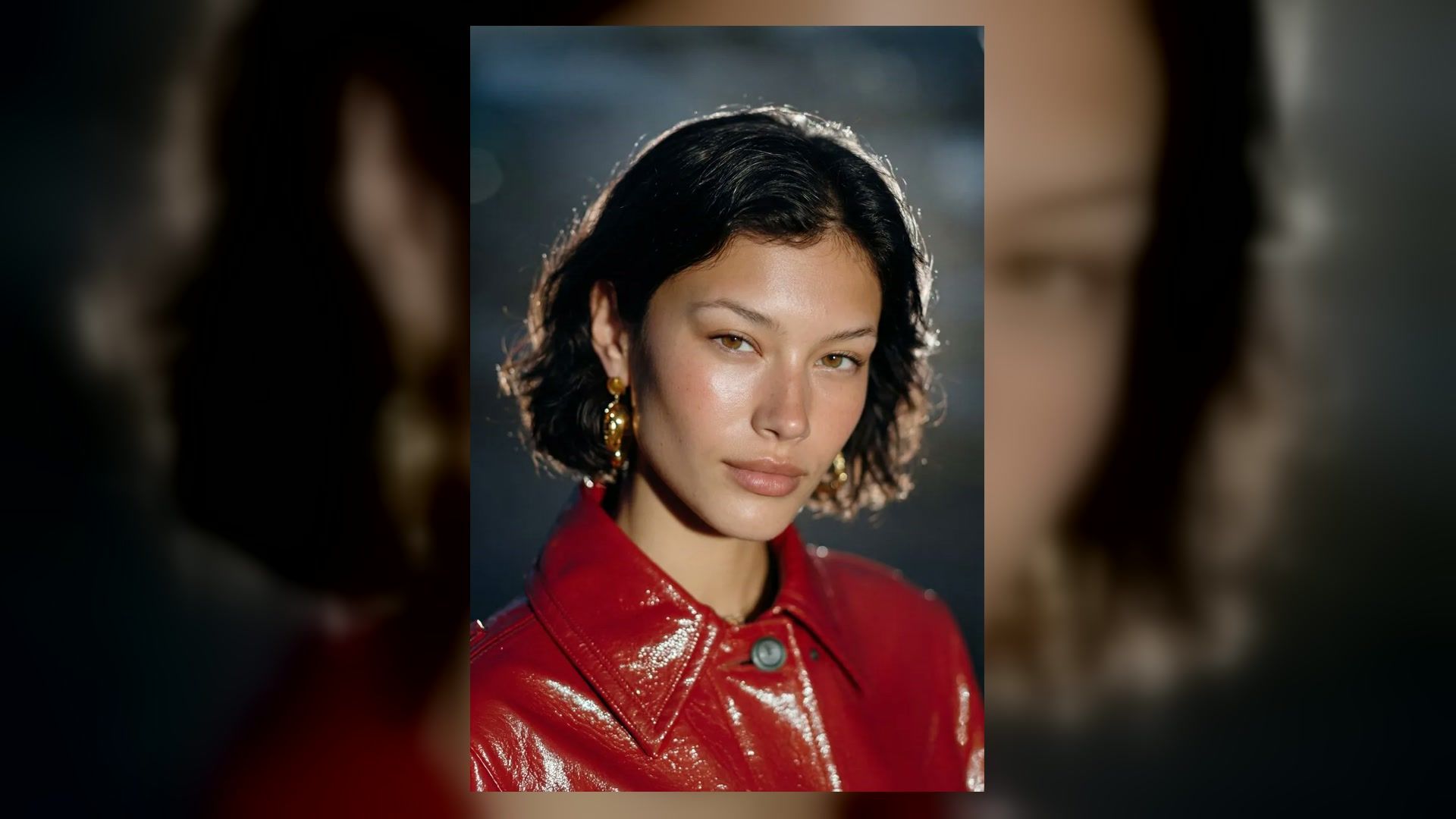 mod-inspired close-up portrait with a short dark bob, gold earrings, and glossy red jacket