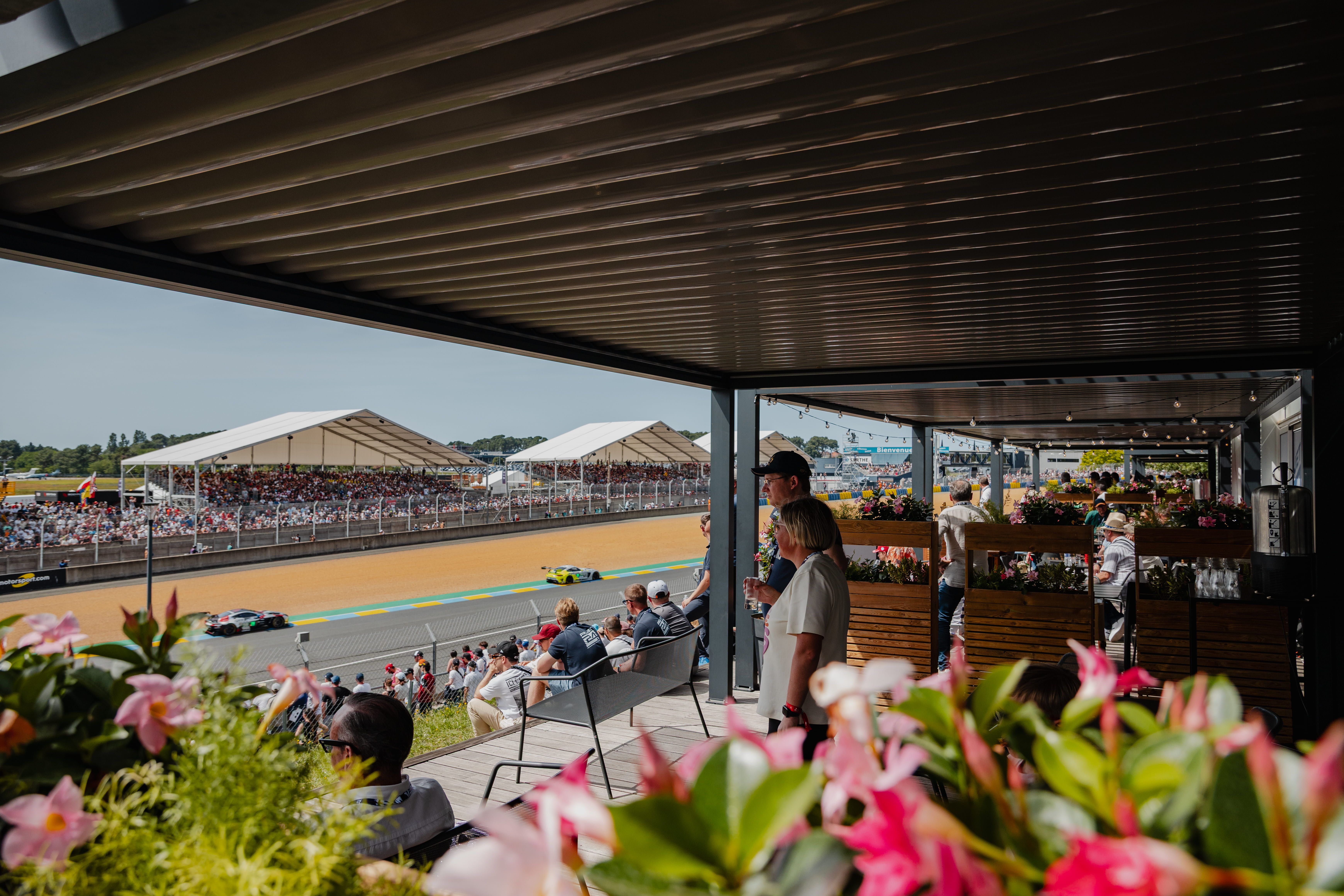 Spectateurs dans un espace d’hospitalité fleuri surplombant la piste et les tribunes des 24 Heures du Mans