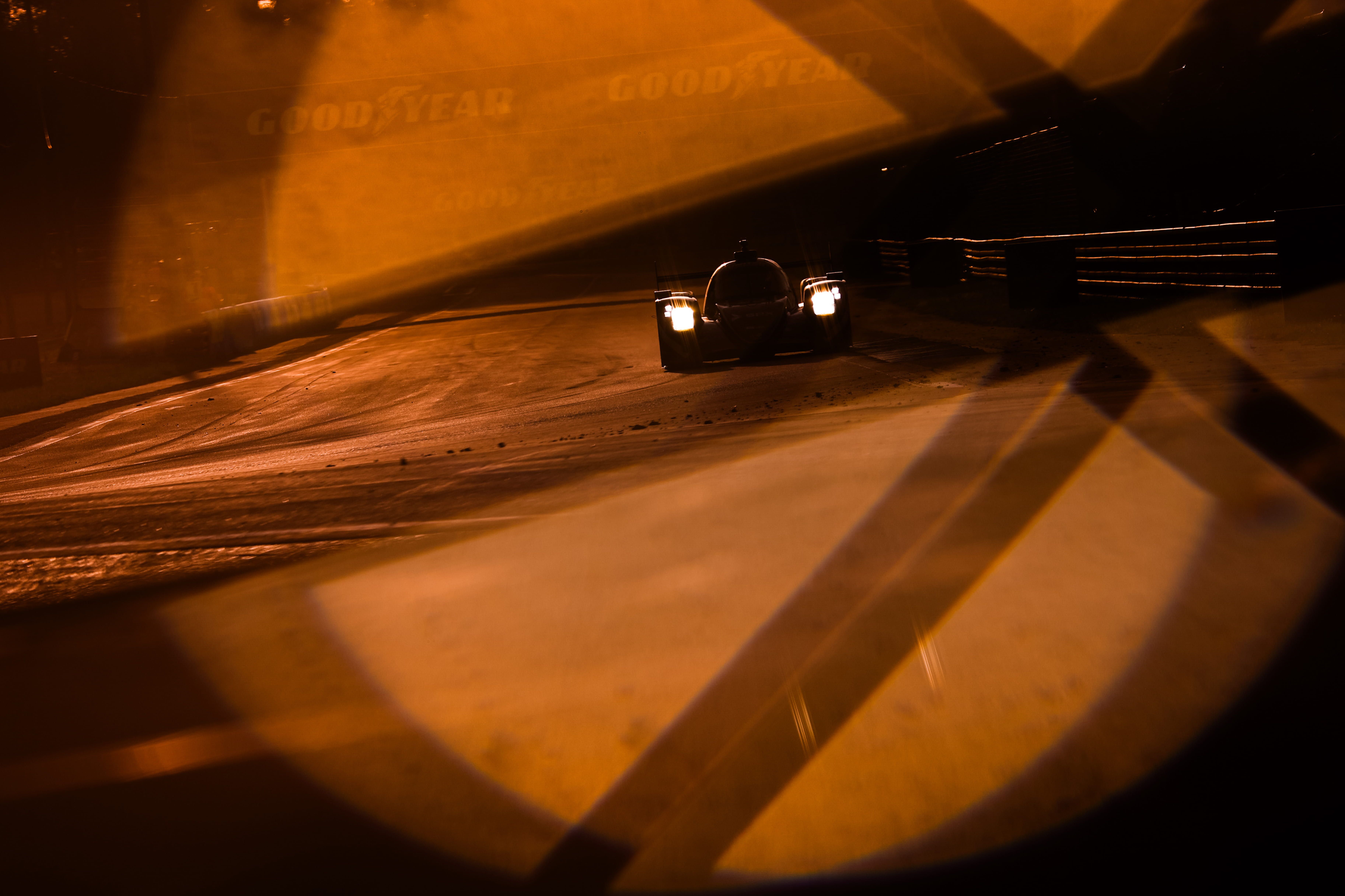 Prototype aux phares allumés sur le circuit des 24 Heures du Mans, baigné d’une lumière orangée