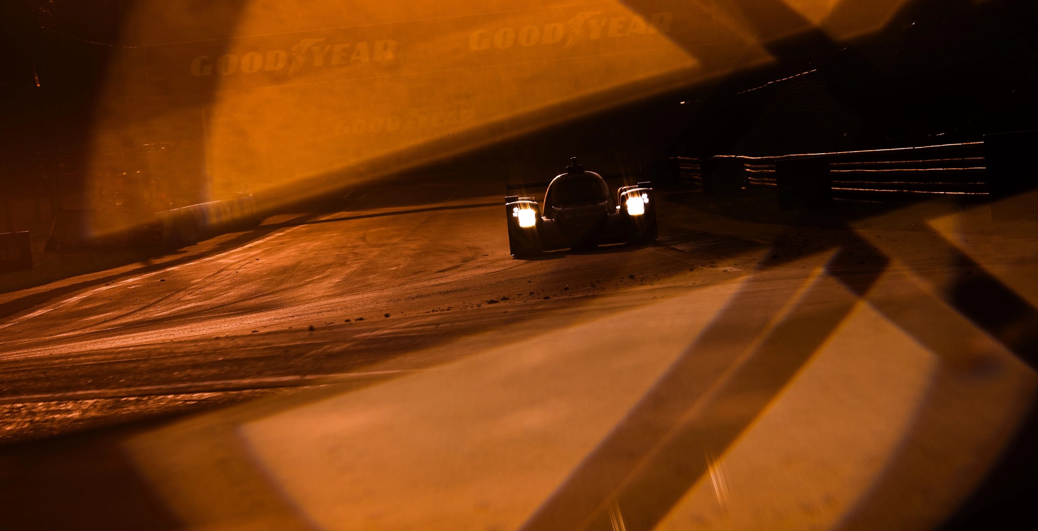 Prototype aux phares allumés sur le circuit des 24 Heures du Mans, baigné d’une lumière orangée