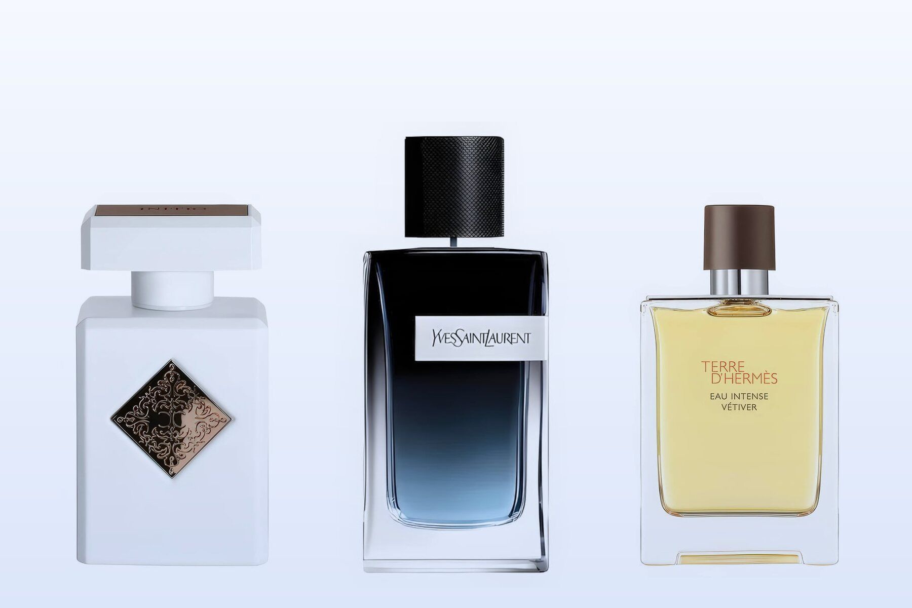 Three bottles on a pale blue background, Paragon by Initio, Y Eau de Parfum by Yves Saint Laurent and Terre d'Hermès Eau Intense Vetiver