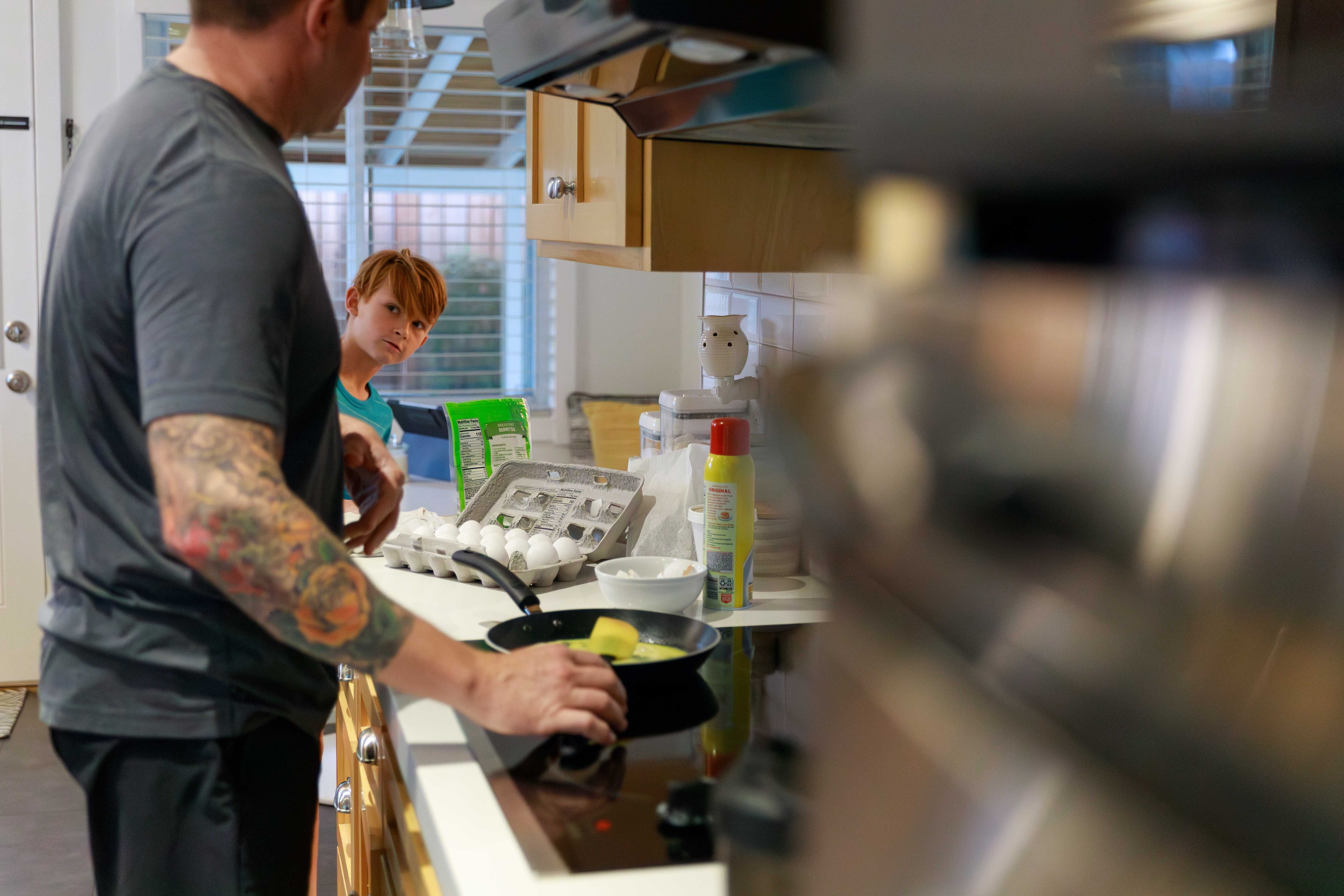 A parent cooking breakfast in a kitchen while a young boy watches