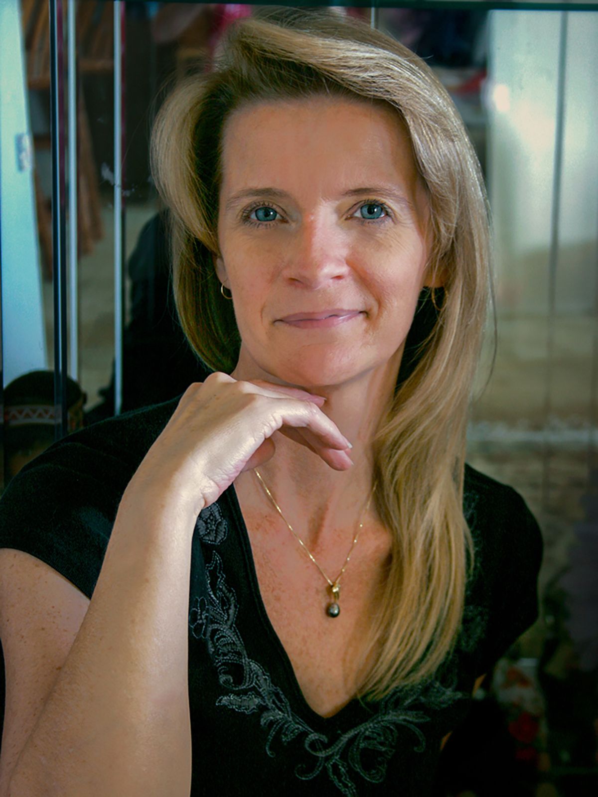 A smiling blonde woman with blue eyes rests her chin on her hand for a portrait, captured by Lavon Photography
