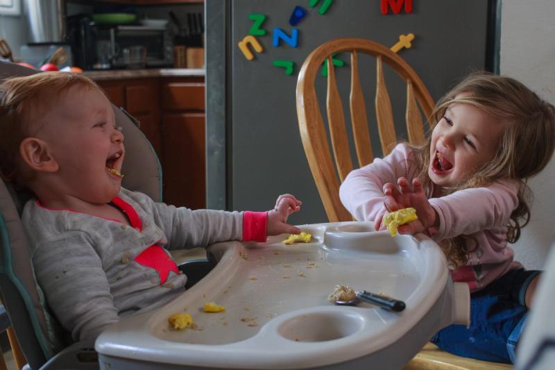 Two toddlers laughing heartily during a messy meal.