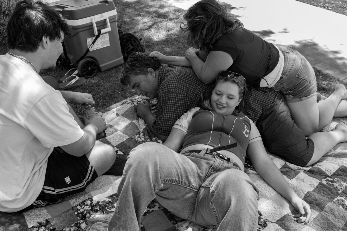 A family relaxes closely together on a picnic blanket outdoors, with a cooler nearby.